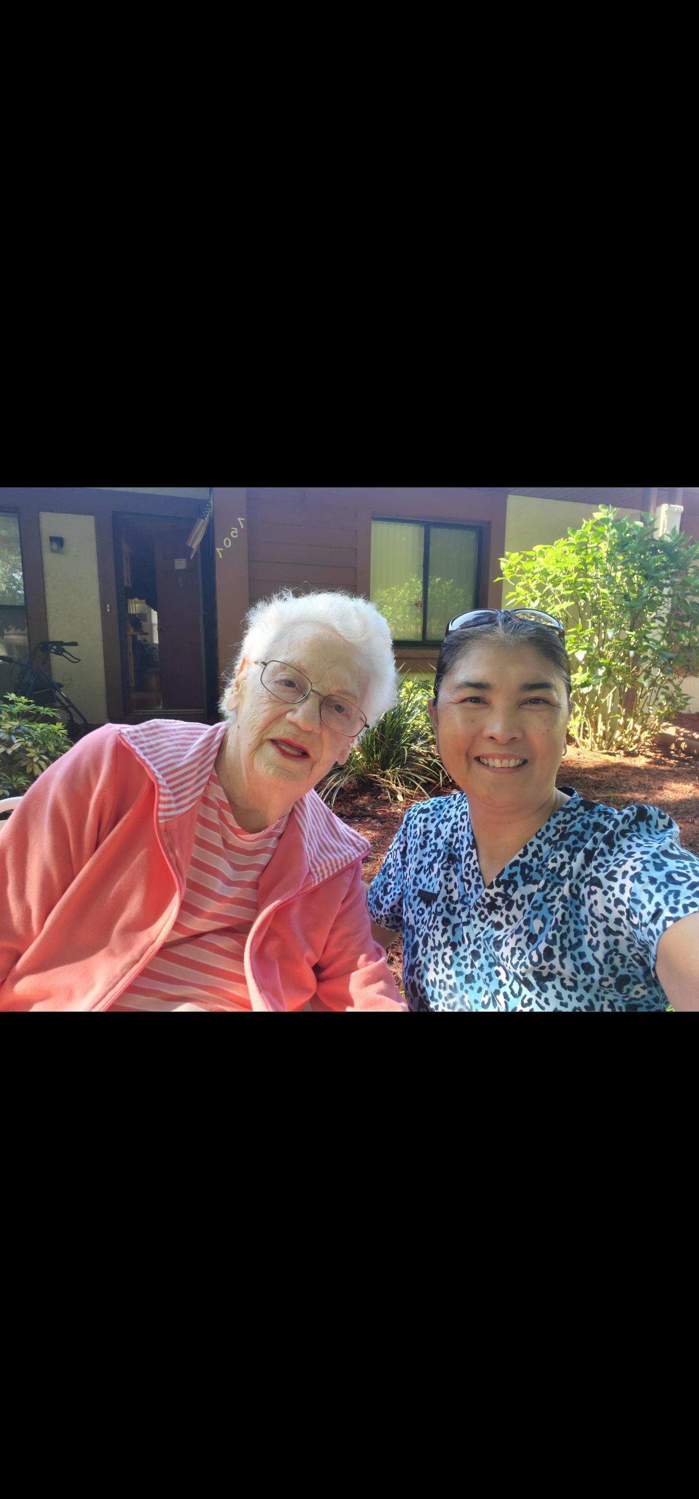 Two women share a joyful moment outdoors in a garden at a residential facility on a sunny day.