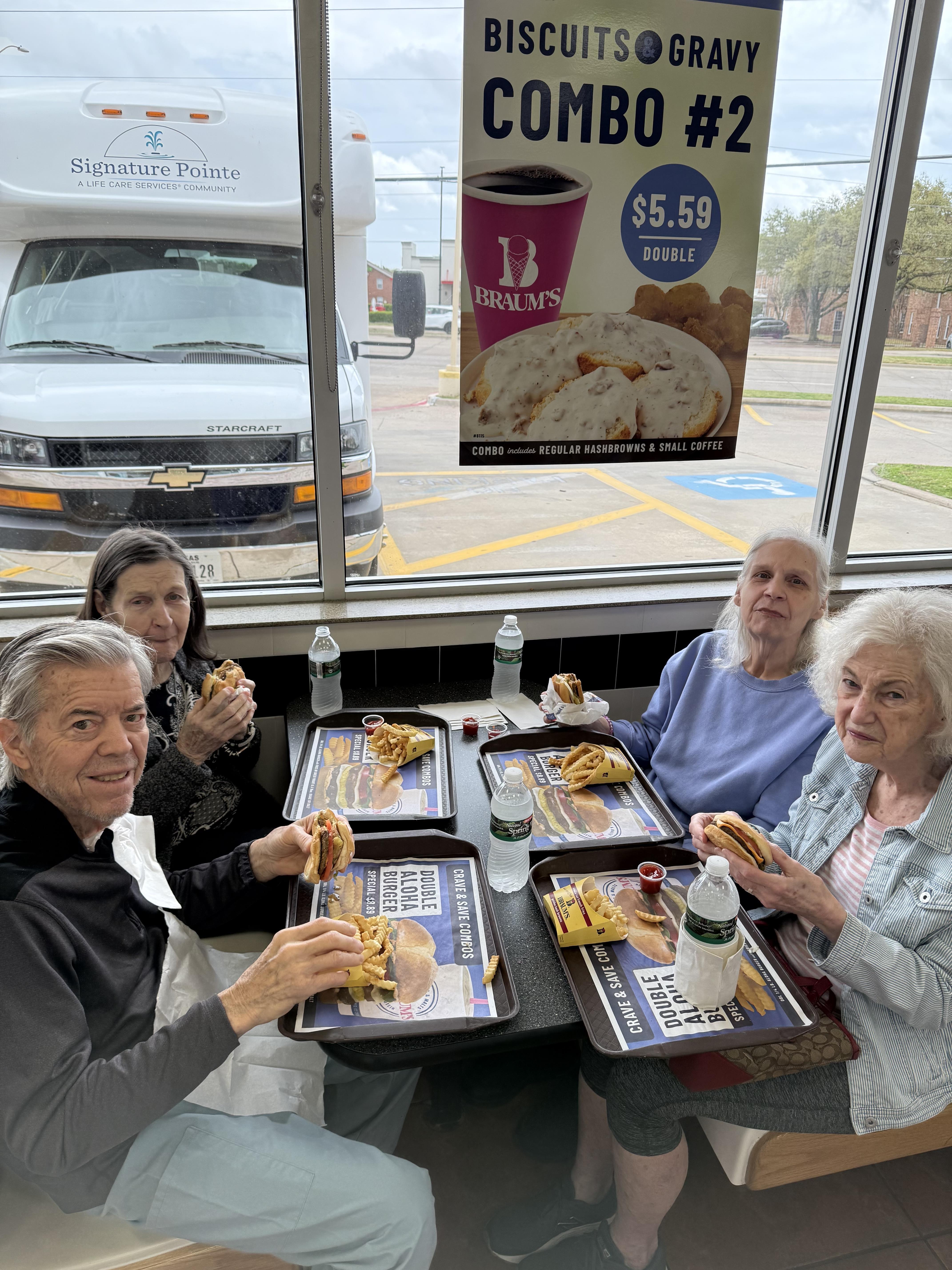Four seniors are sharing a meal at a diner with bright natural light illuminating their table.