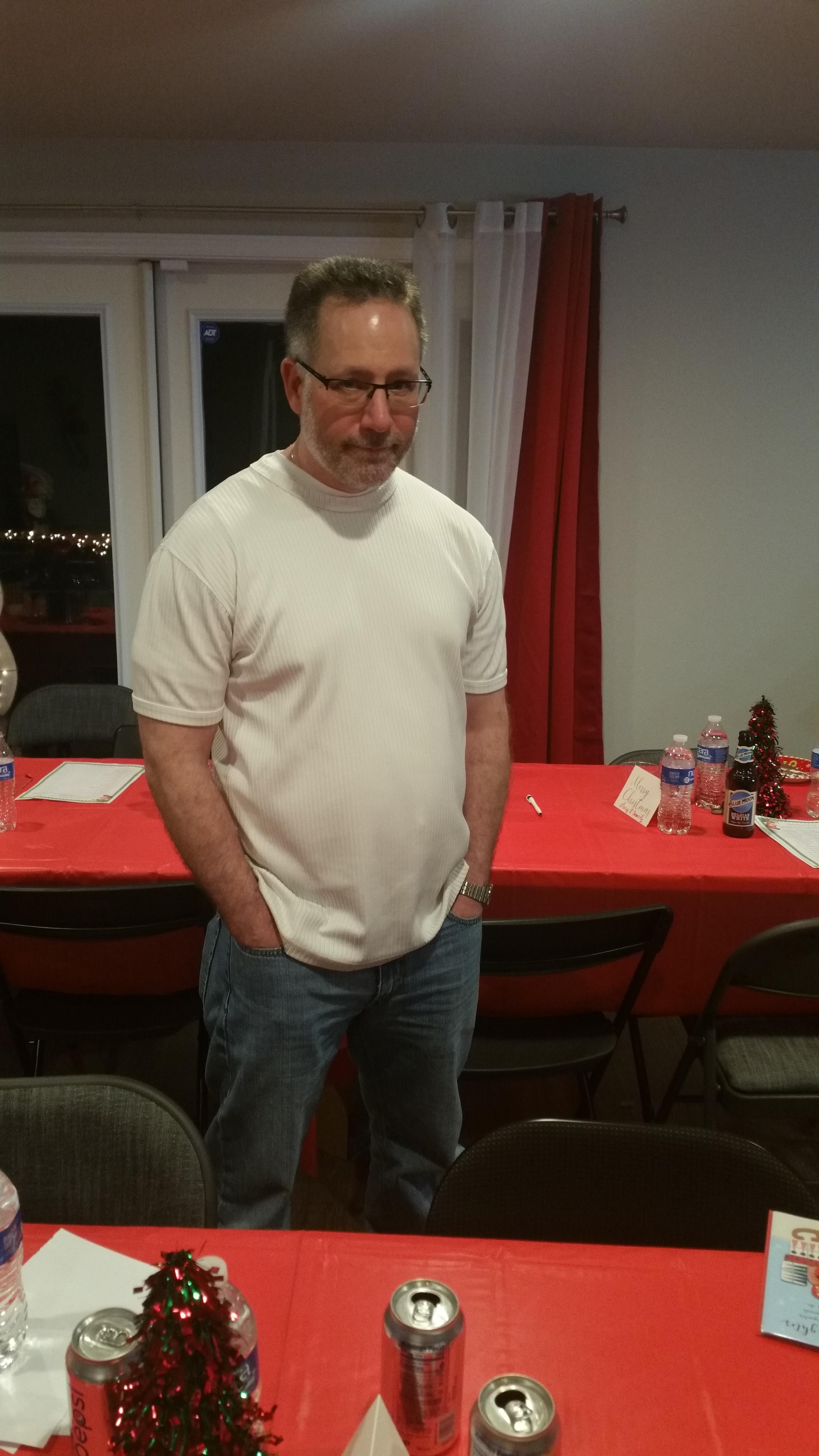 A man stands casually with his hands in his pockets beside a decorated table during a gathering.