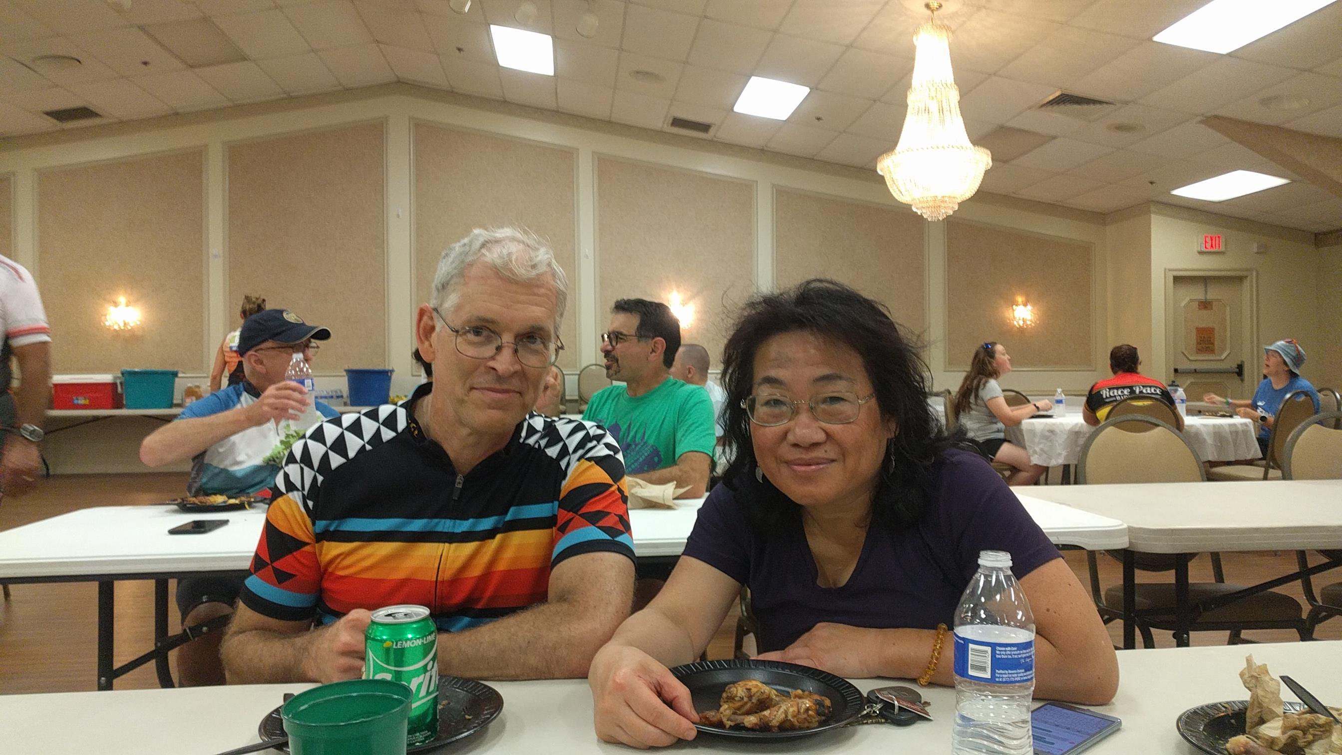 Two individuals sit at a table, sharing food and enjoying each other's company during an event.