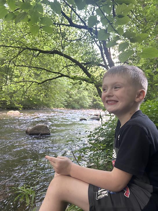 A boy sitting on a rock near a river