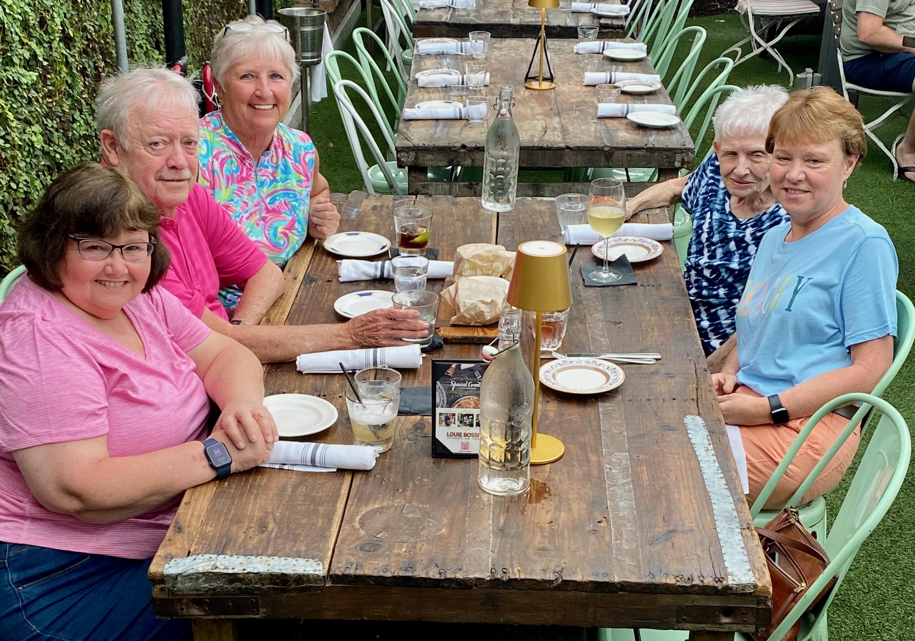 Friends gather around a long wooden table sharing laughter and enjoying delicious food and drinks.