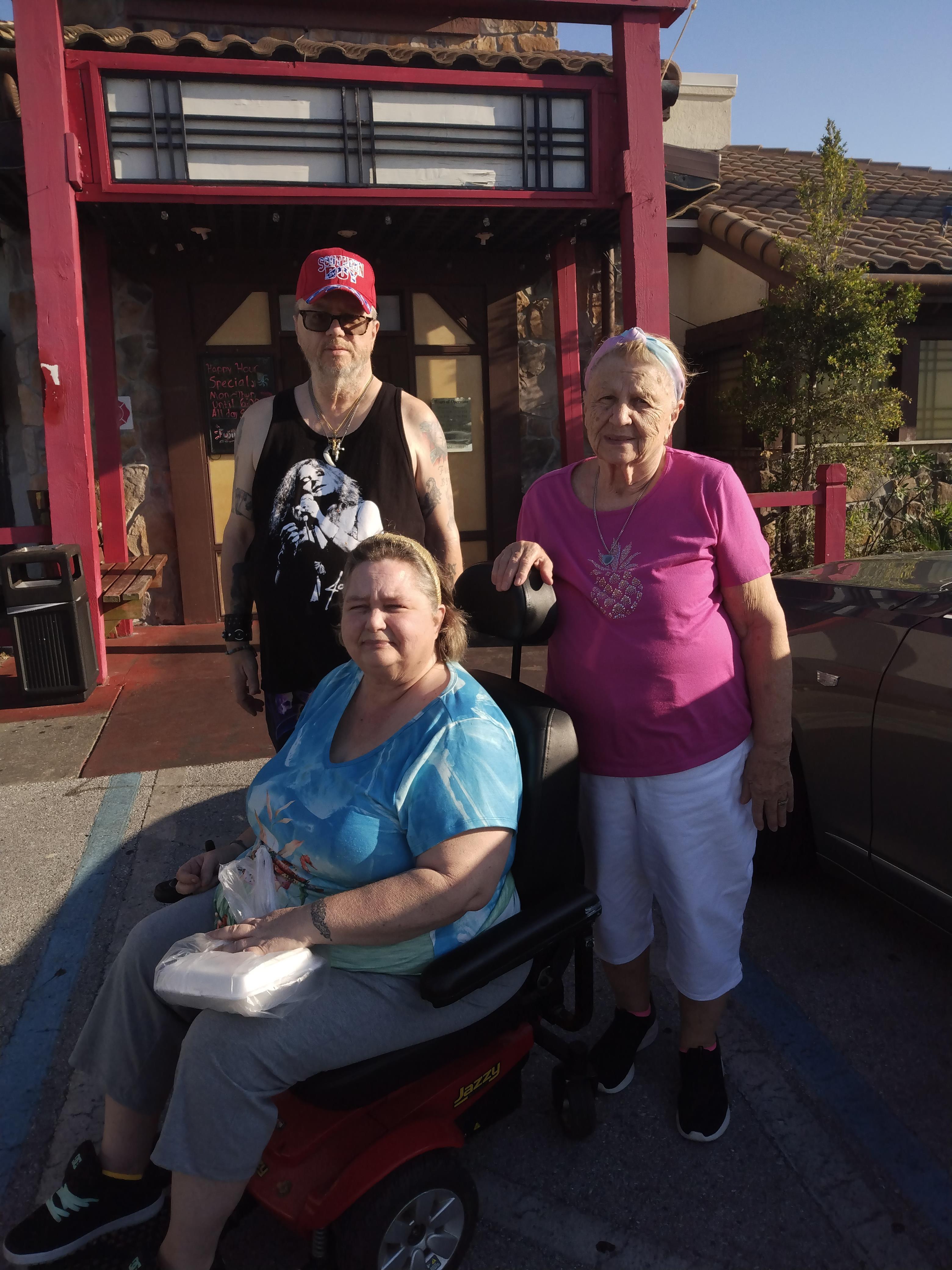 Three friends gather outside a restaurant, enjoying the sunshine and each other's company.