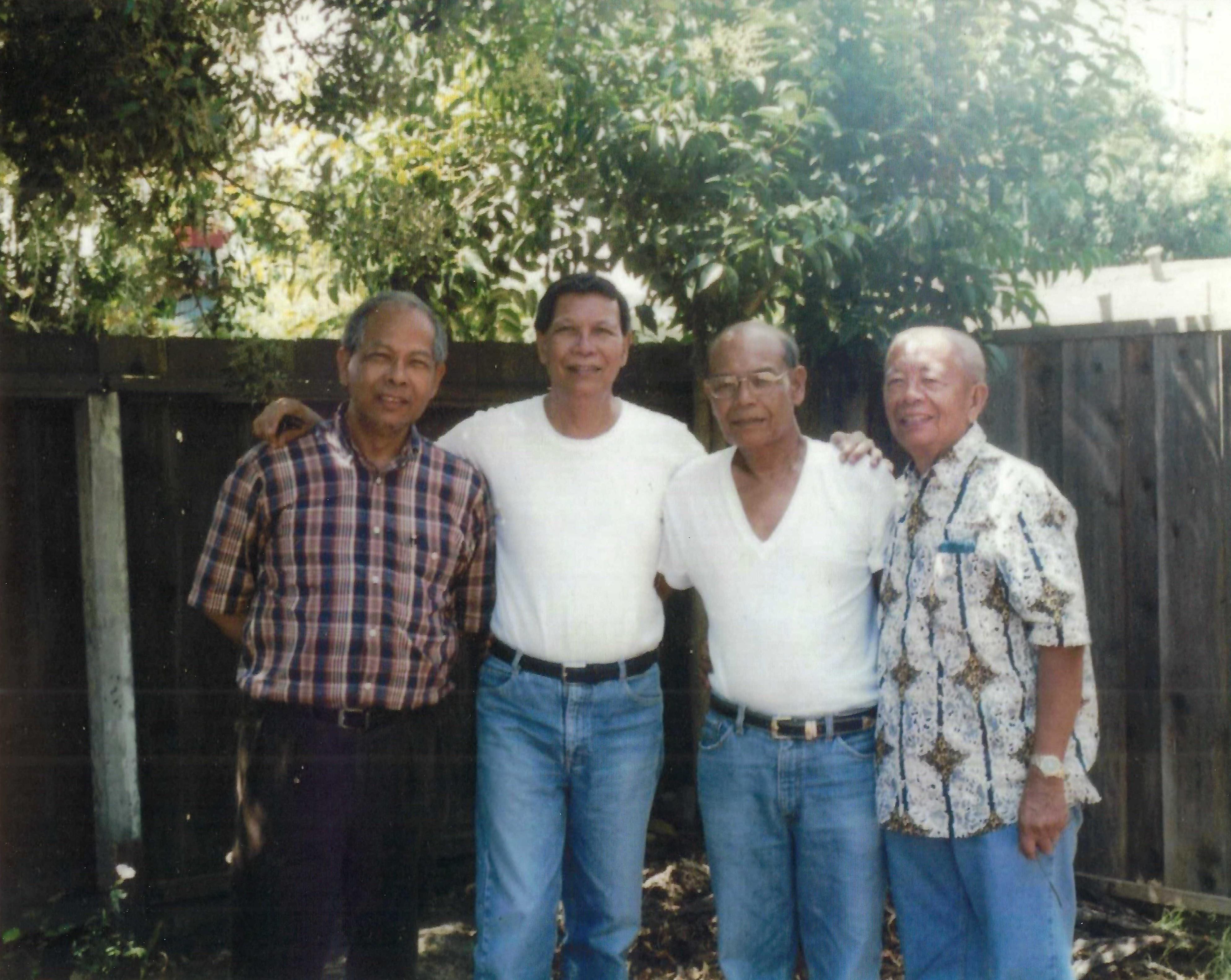 Four men stand together in a garden, smiling and connecting in a relaxed, sunny atmosphere.