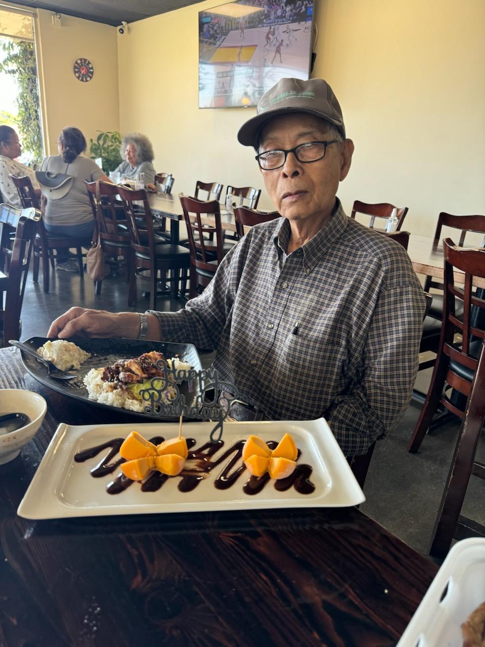 A senior man relishes a delicious meal with dessert in a lively restaurant, surrounded by friends.