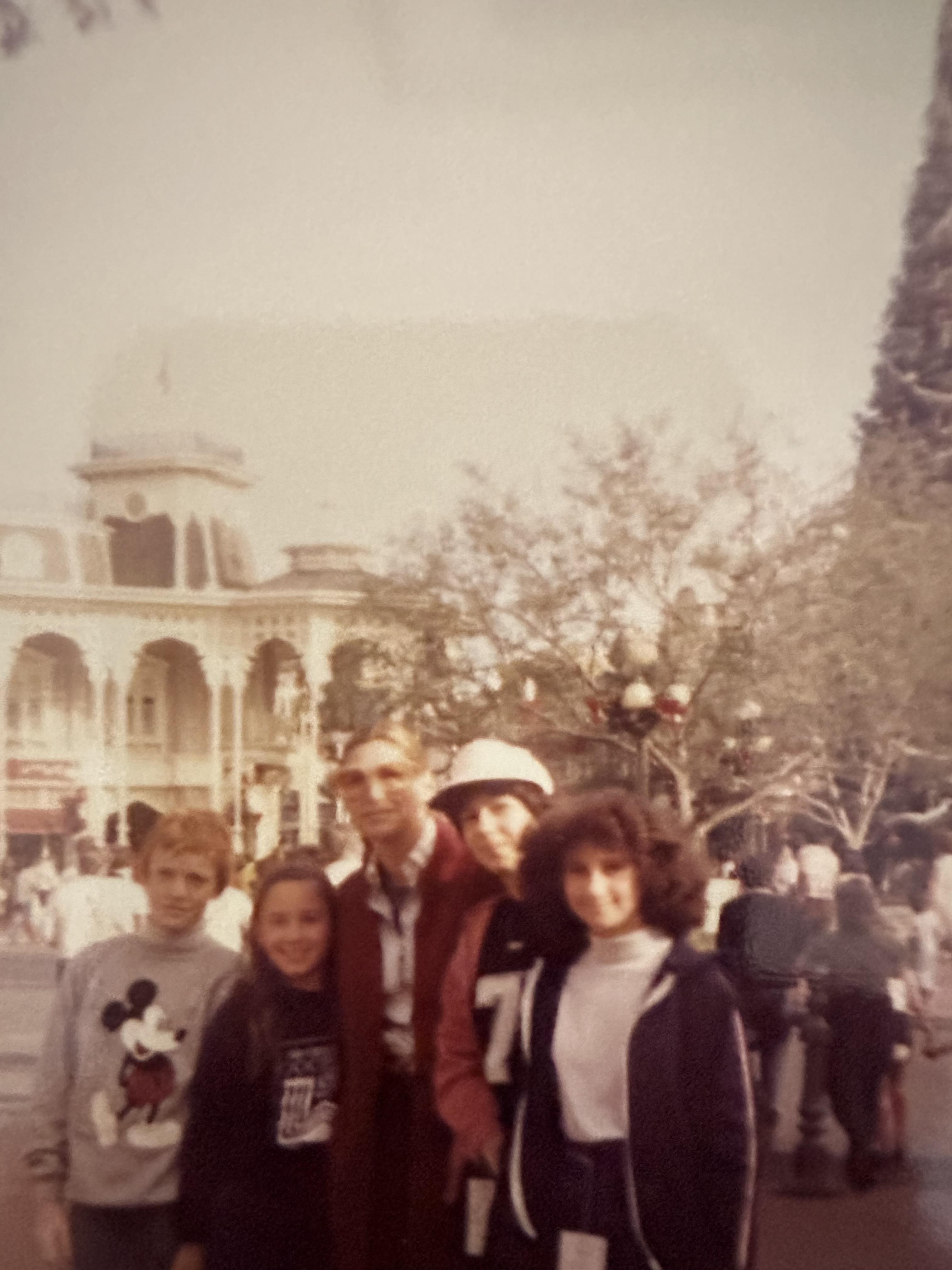 Five people smile by a historic building, enjoying their time at the amusement park.