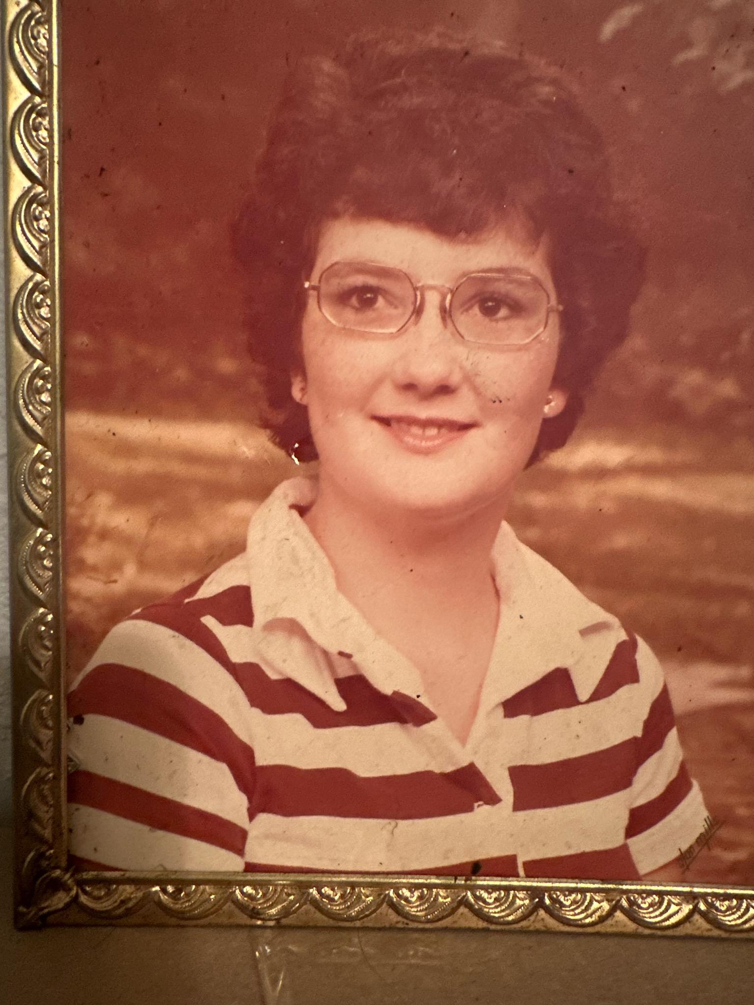 Cheerful young girl poses for a portrait outdoors, wearing glasses and a striped shirt.