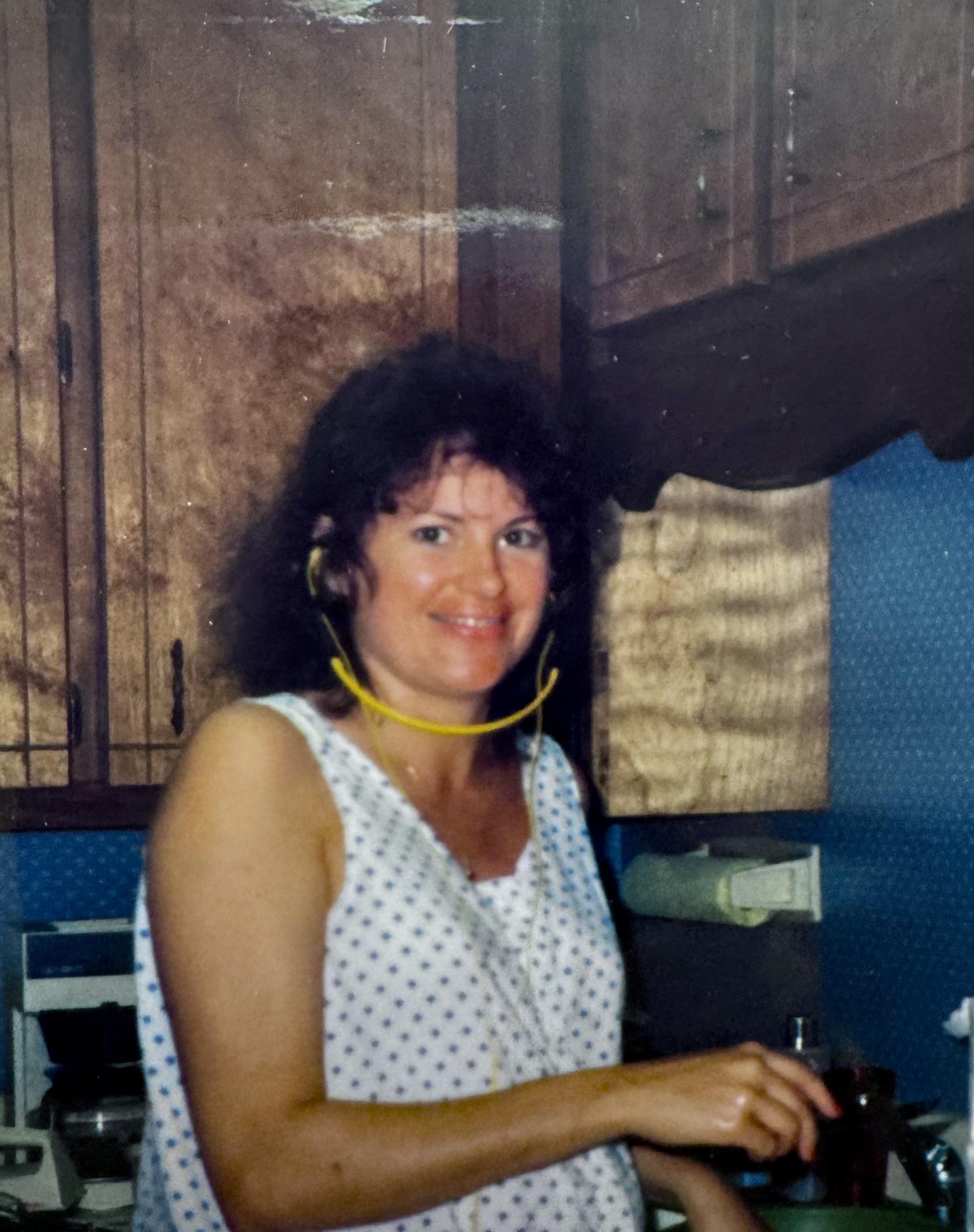 A woman with curly hair happily cooks in her kitchen, smiling as she prepares a meal.