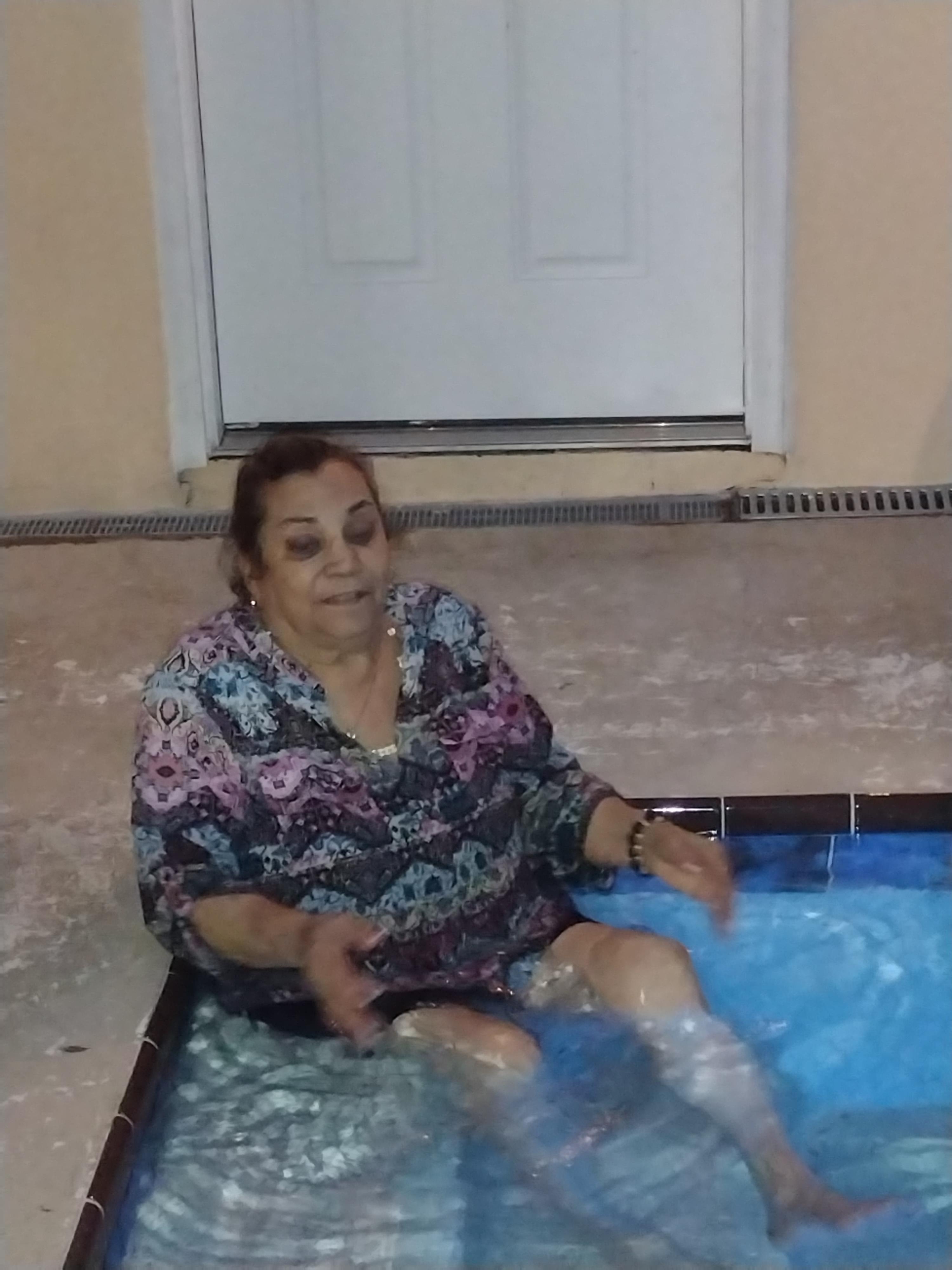 A woman sits comfortably in a small pool, immersed in water, visibly enjoying her time at home.