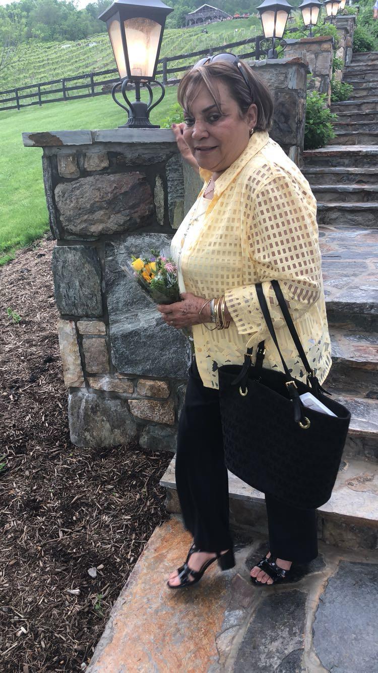 Elderly woman enjoys a sunny day at home, holding a bouquet of flowers near stone steps.