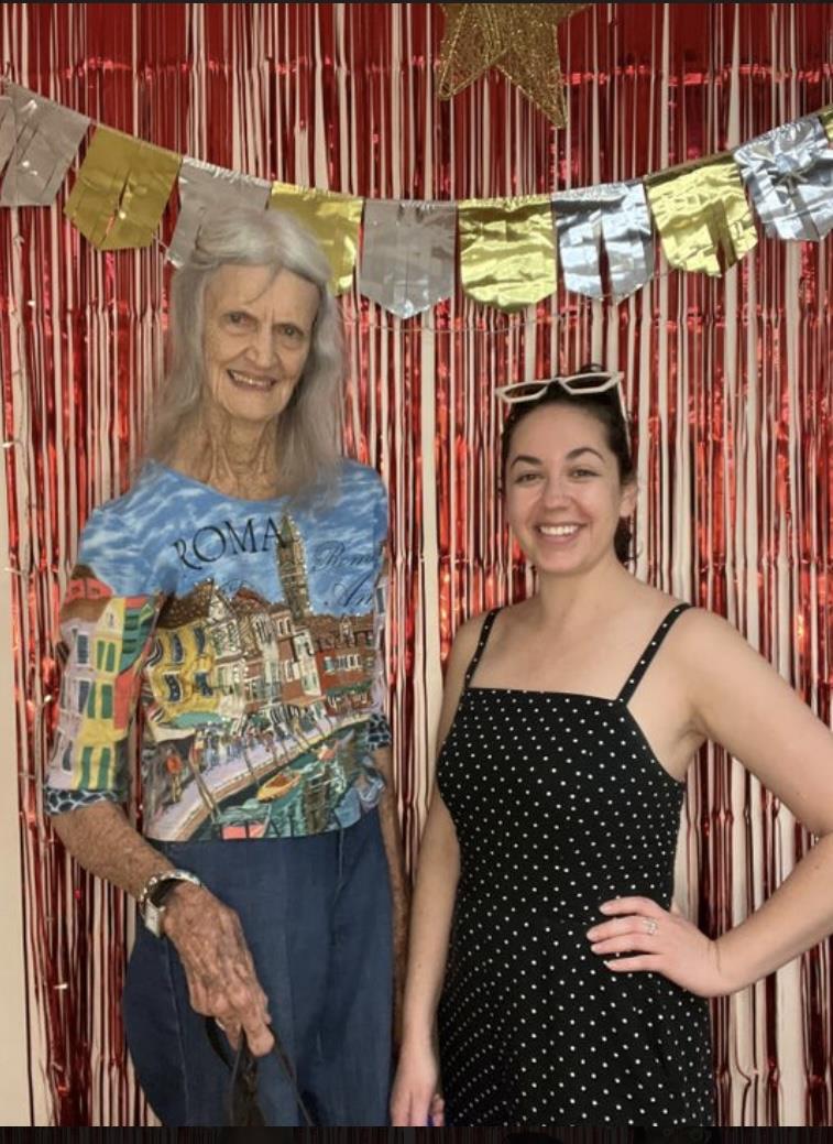 A woman beams next to her elderly friend at a festive gathering with vibrant decorations.