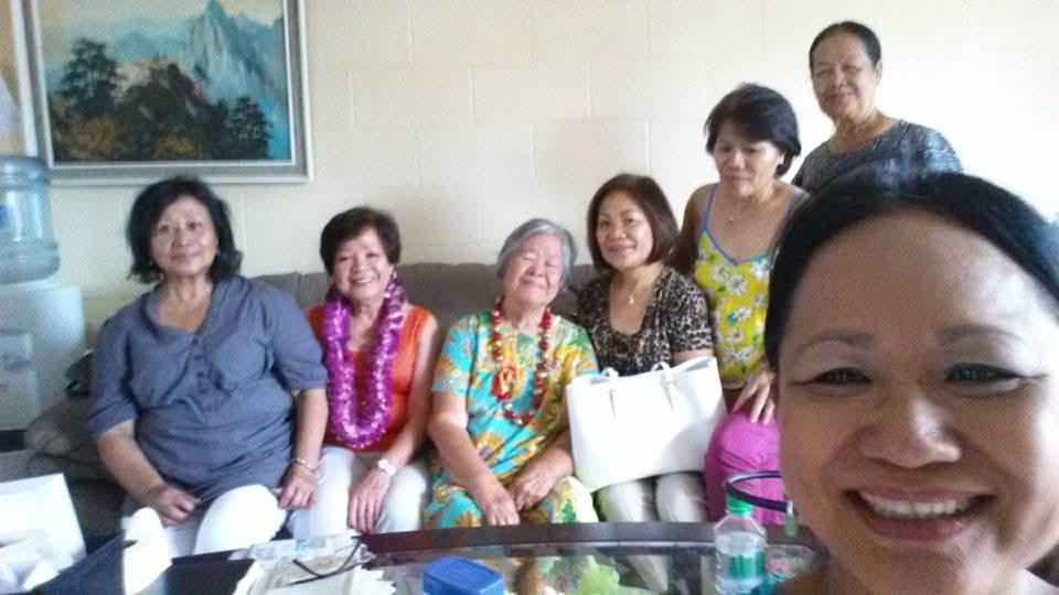 Seven women and one man smile together in a cozy living room, celebrating their friendship.