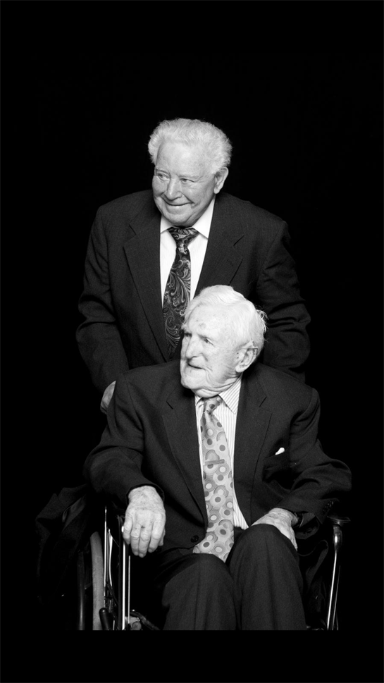 A man in a suit and tie standing next to a man in a wheelchair
