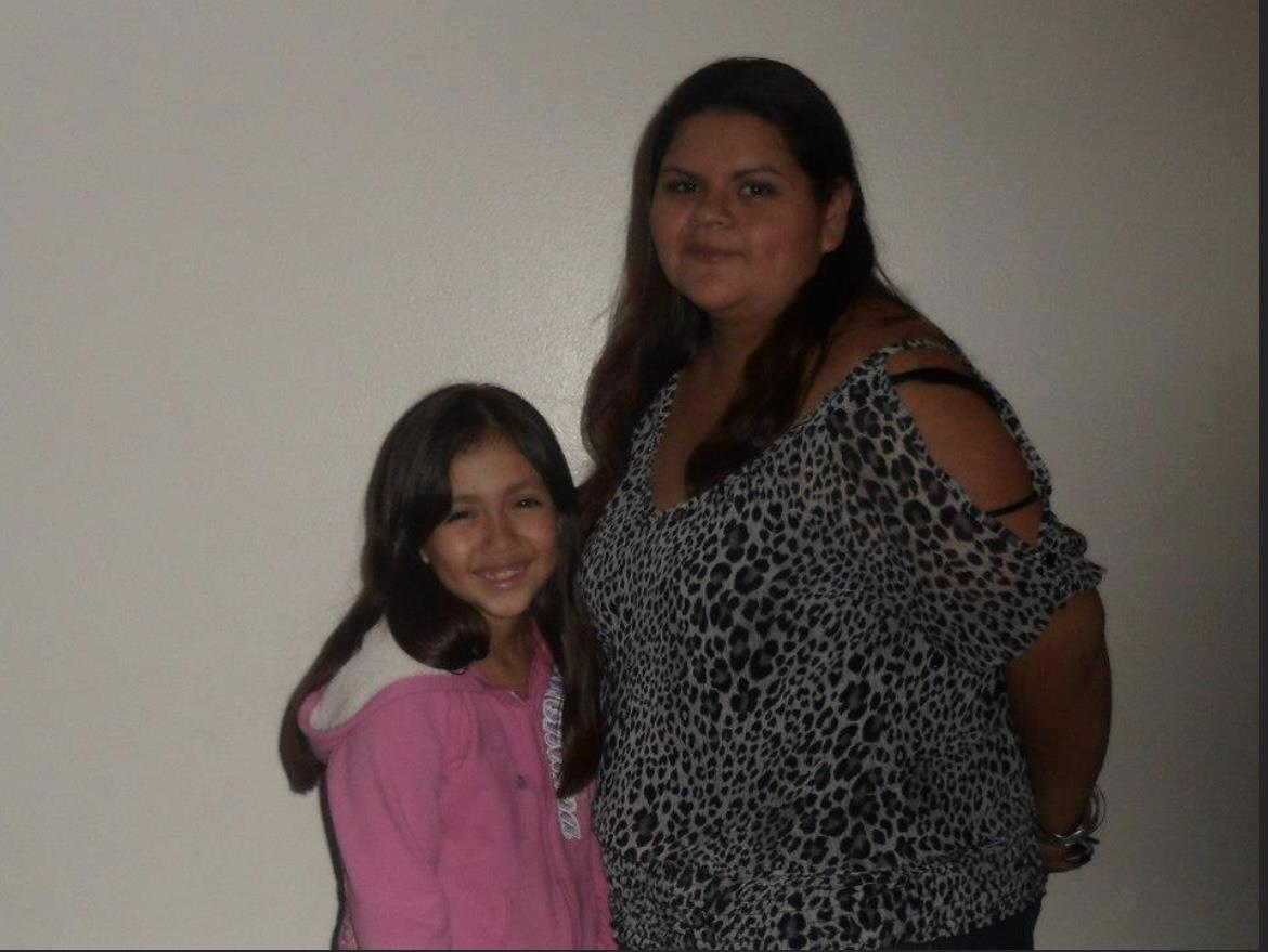 A woman and a girl stand close together with smiles, showcasing their bond and joy indoors.