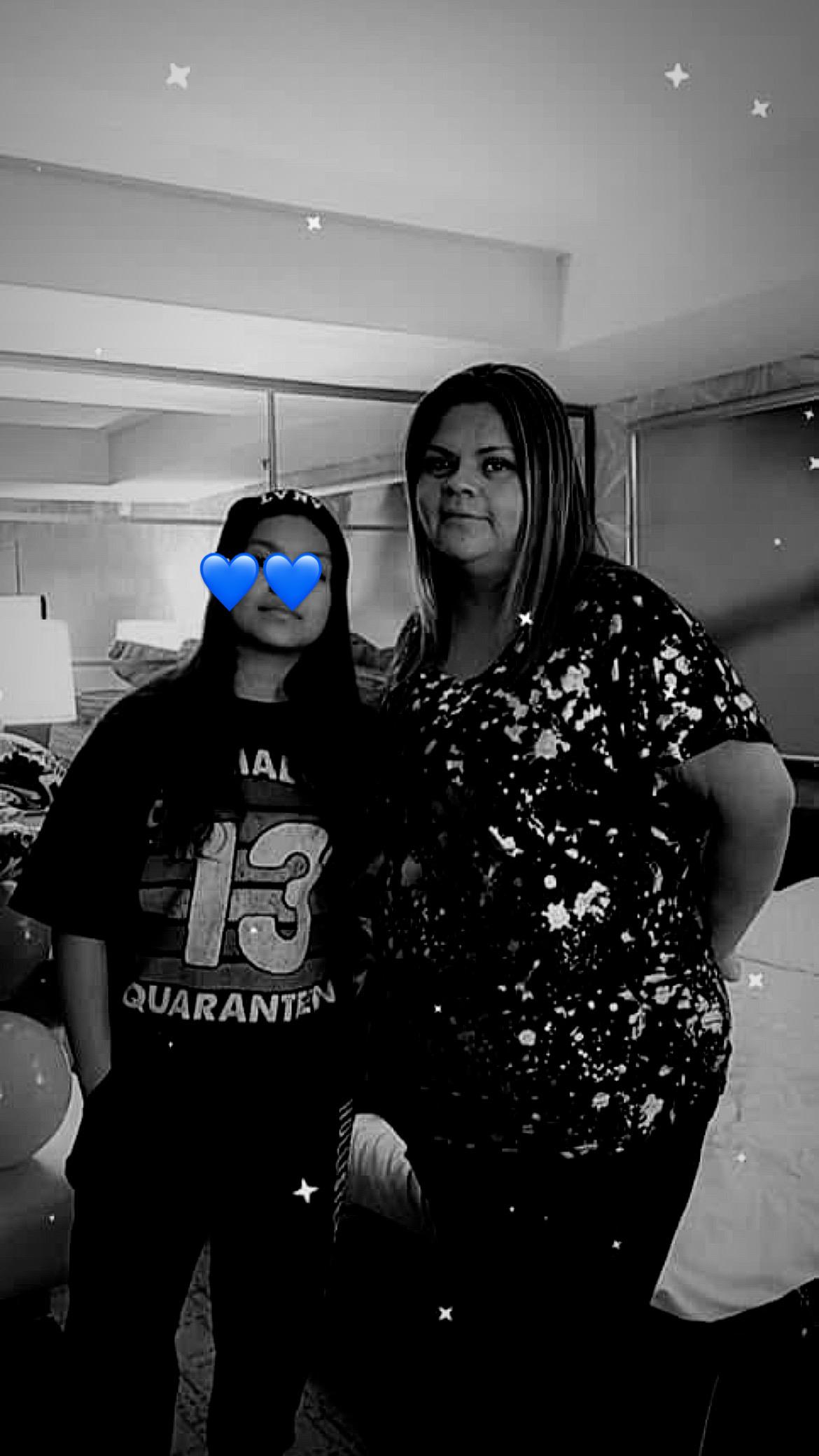 Two women stand together, smiling in a comfortable indoor setting, showcasing a joyful moment.