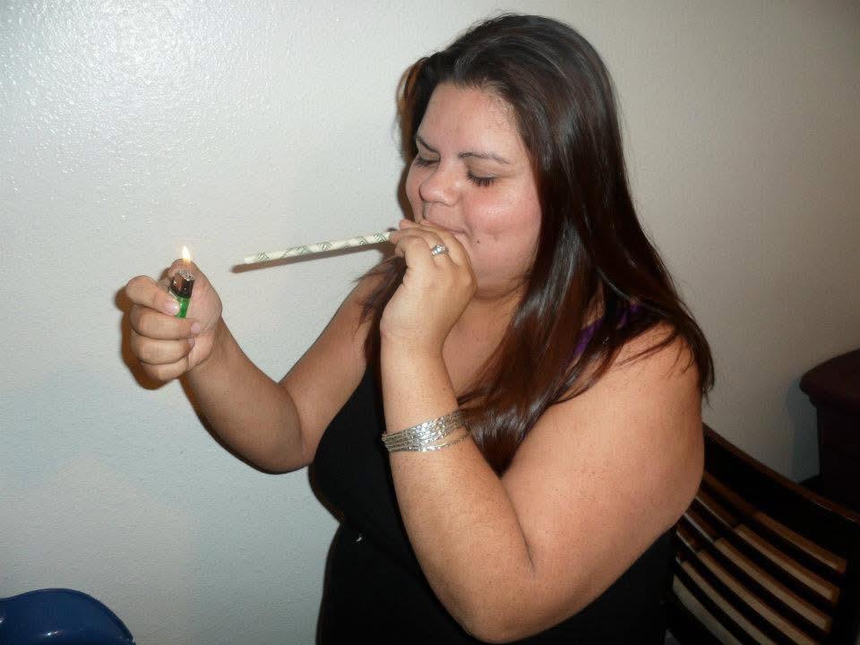 A woman with long hair lights a smoke stick, appearing relaxed in a cozy indoor atmosphere.
