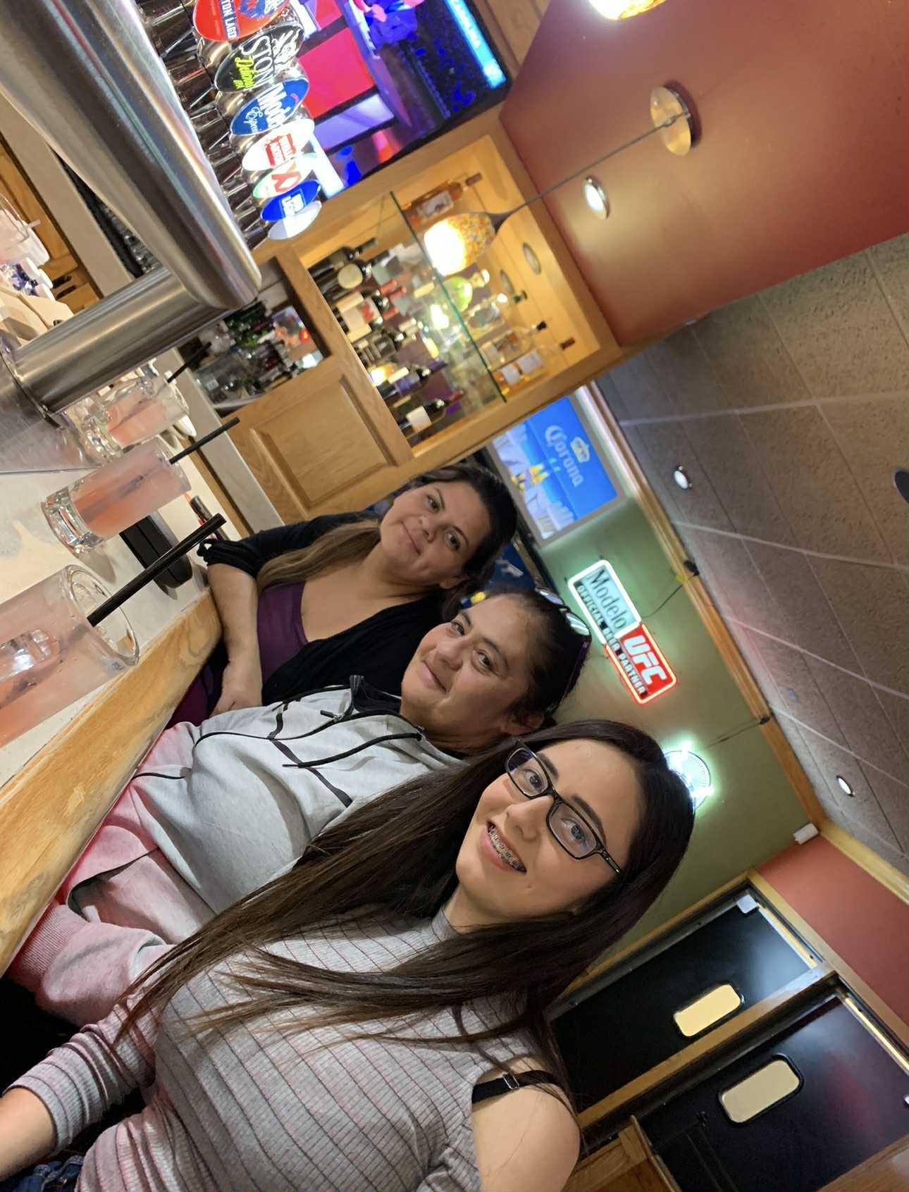 Three friends smile and chat while seated at the bar, enjoying drinks and each other's company.