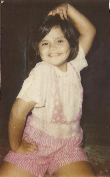 A cheerful girl in a pink outfit showcases her playful spirit in a joyful moment.