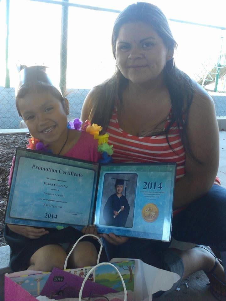 Mother and daughter proudly show off graduation certificates in a sunny outdoor setting.