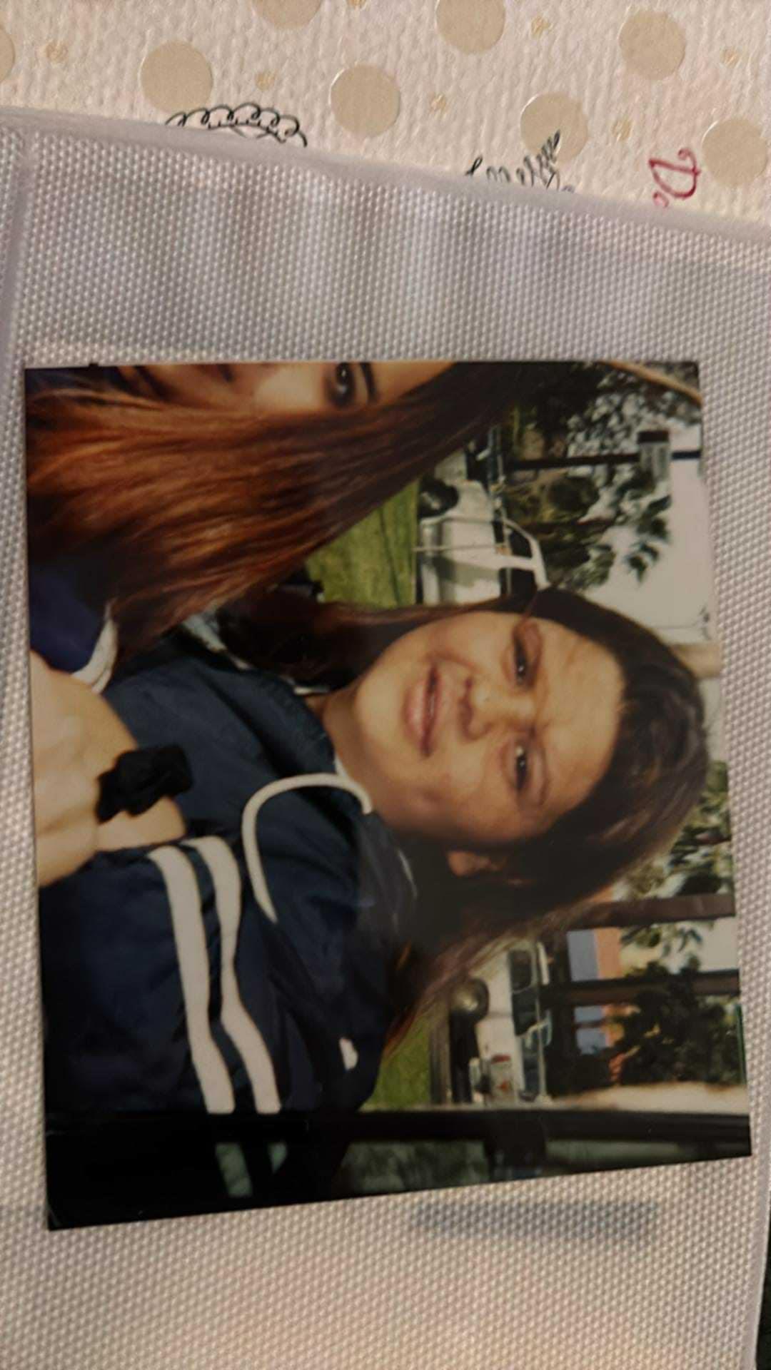 Two friends smile for a picture in a park surrounded by greenery and bright sunshine.