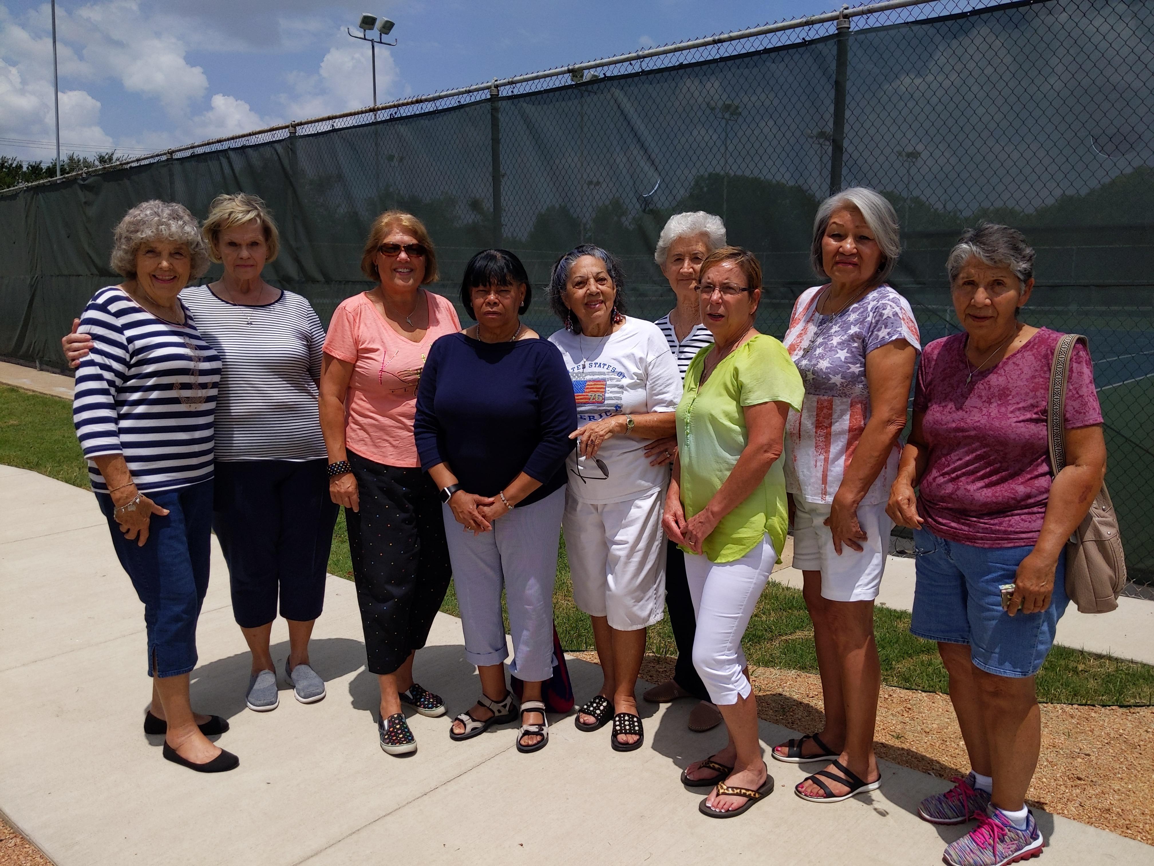 A lively group of women stands together, smiling and enjoying their time at a community park.