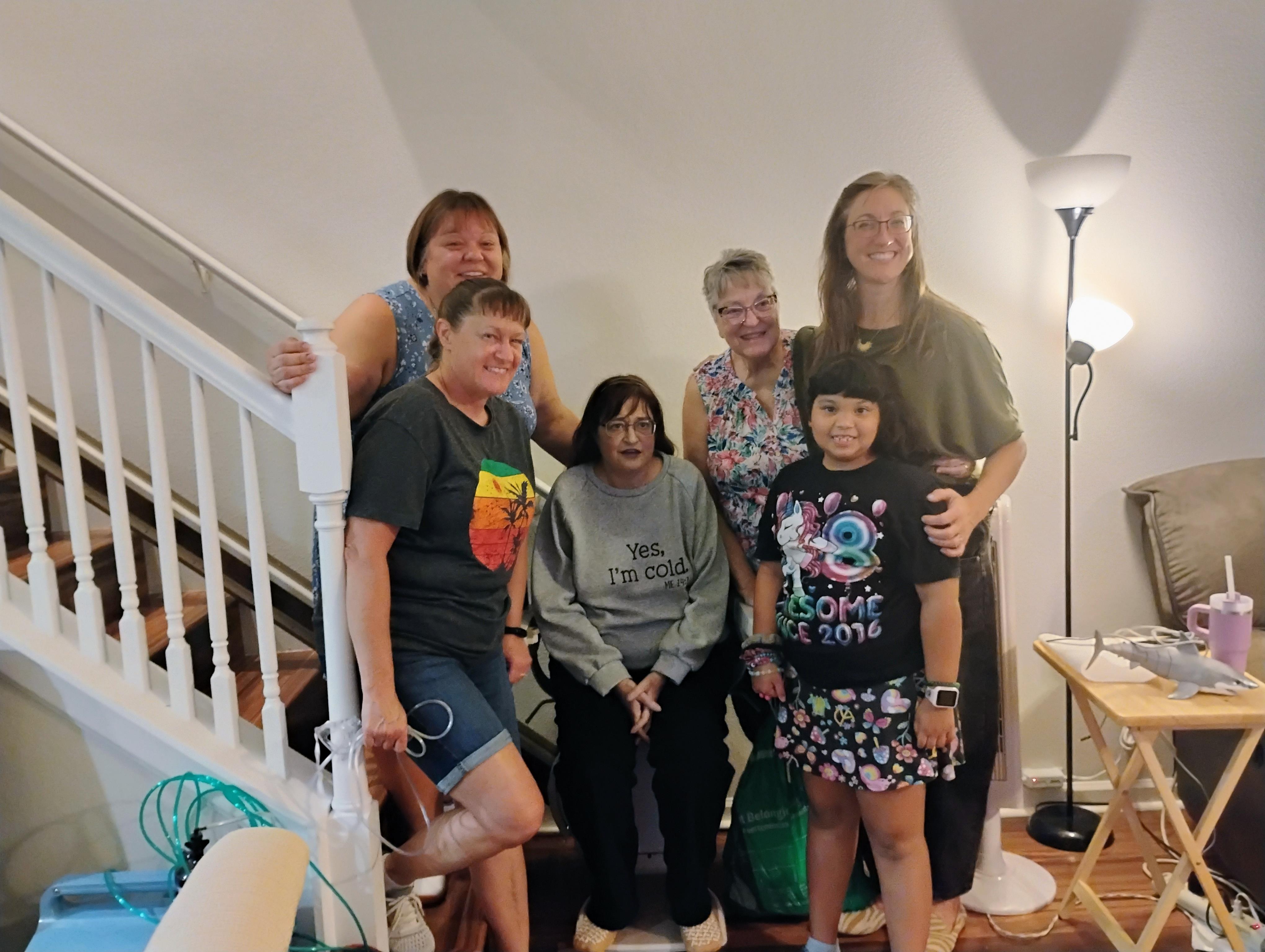 A group of six family members smiles together on a staircase, celebrating their time together.