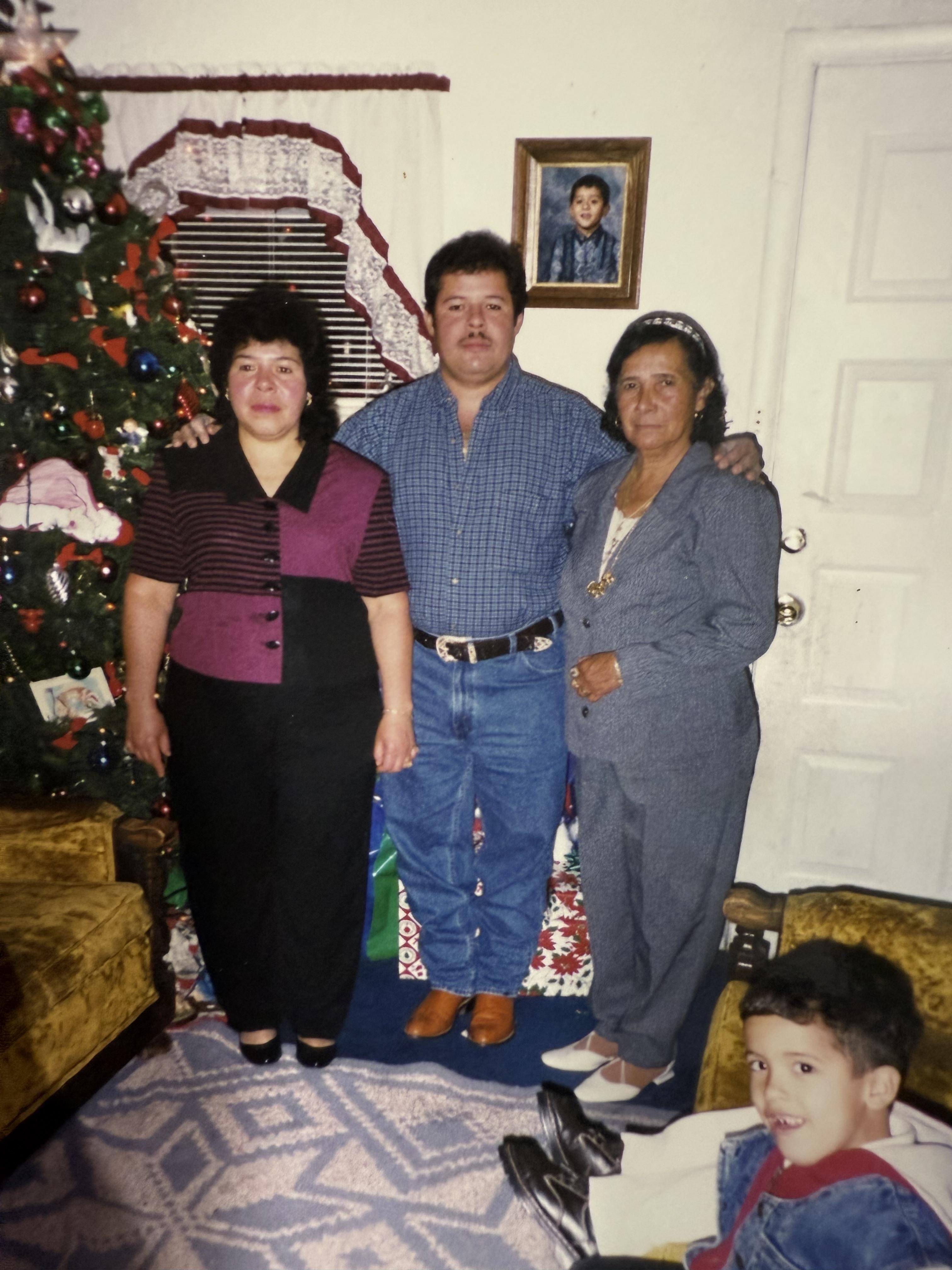 Three adults pose together in front of a festive Christmas tree and decorations, celebrating.