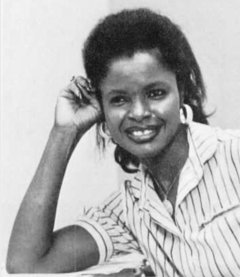 A woman with natural hair shows a joyful smile while resting her hand on her head.