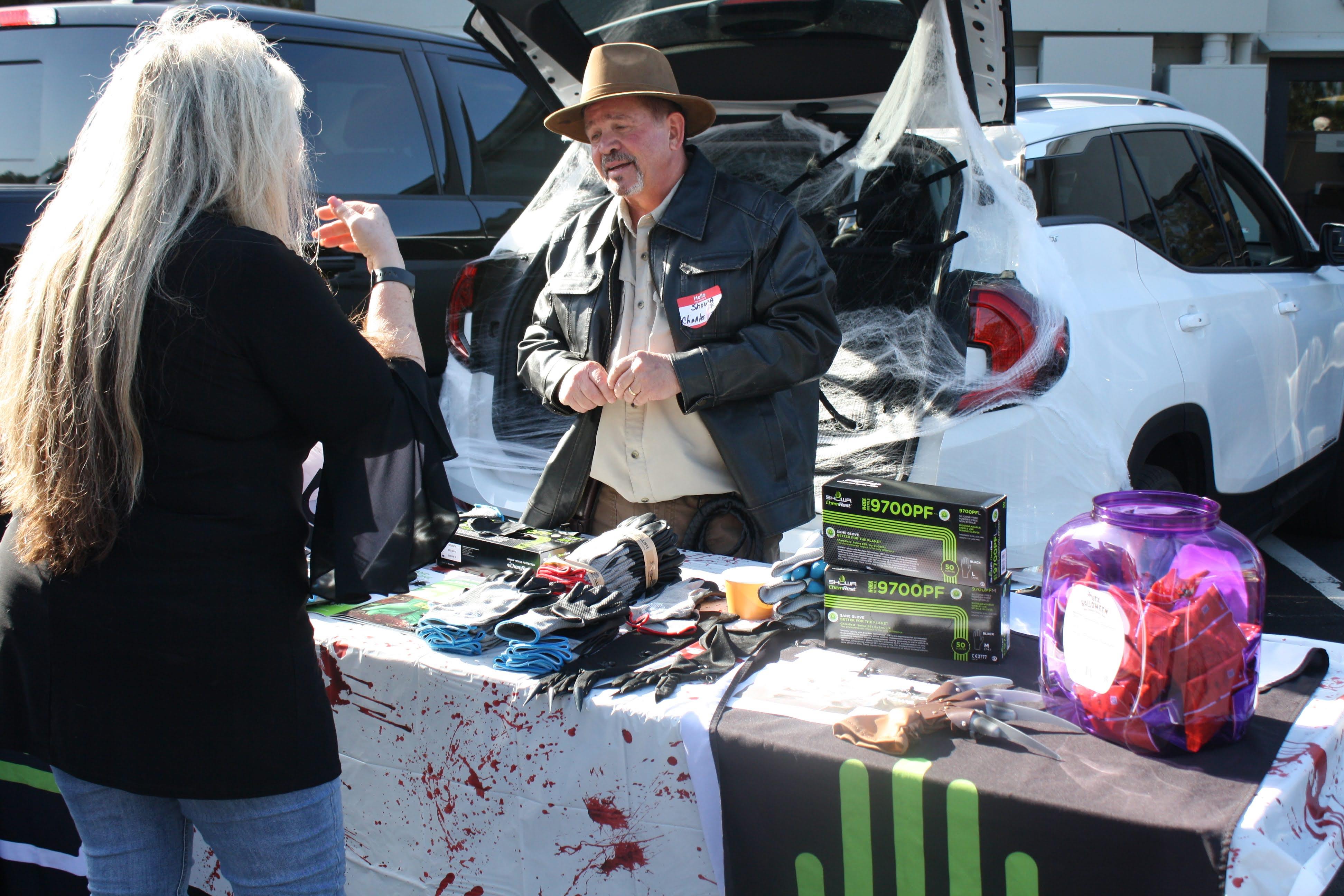 A vendor in a hat sells Halloween decorations to a customer at an outdoor market.