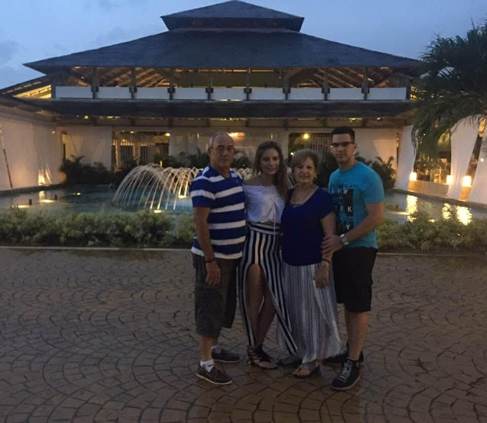 A family poses happily in front of a tropical resort with elegant fountains as twilight falls.