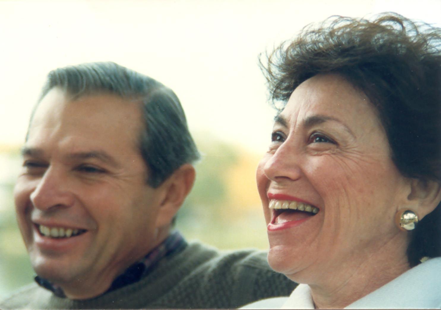 Two older adults laugh joyfully together in a bright, happy indoor setting.