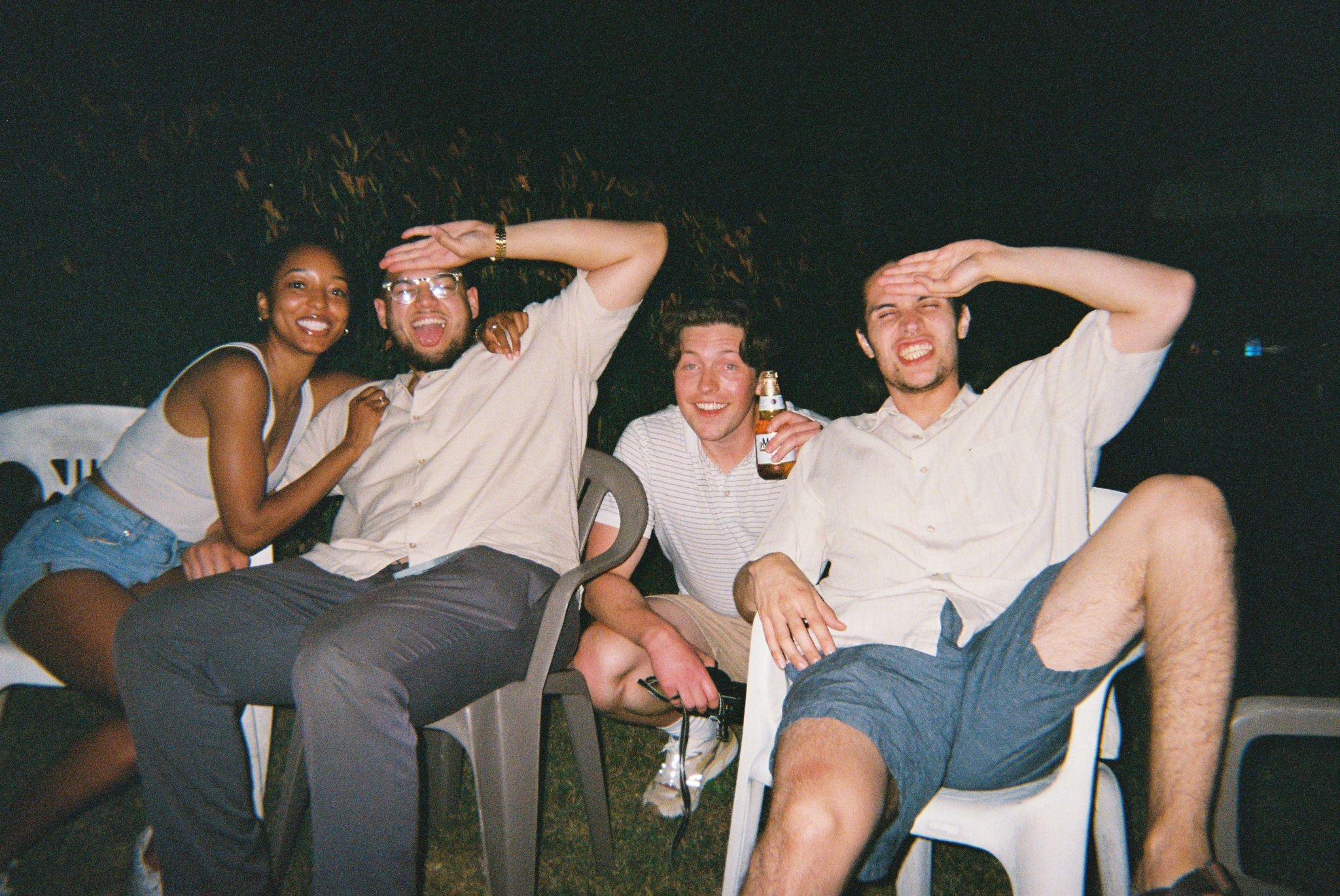 Four friends gather for a fun night, laughing and relaxing with drinks on a warm evening outside.