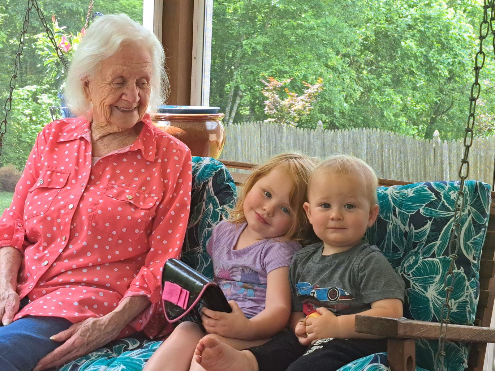 An elderly woman smiles warmly with two children, sharing a joyful family moment.