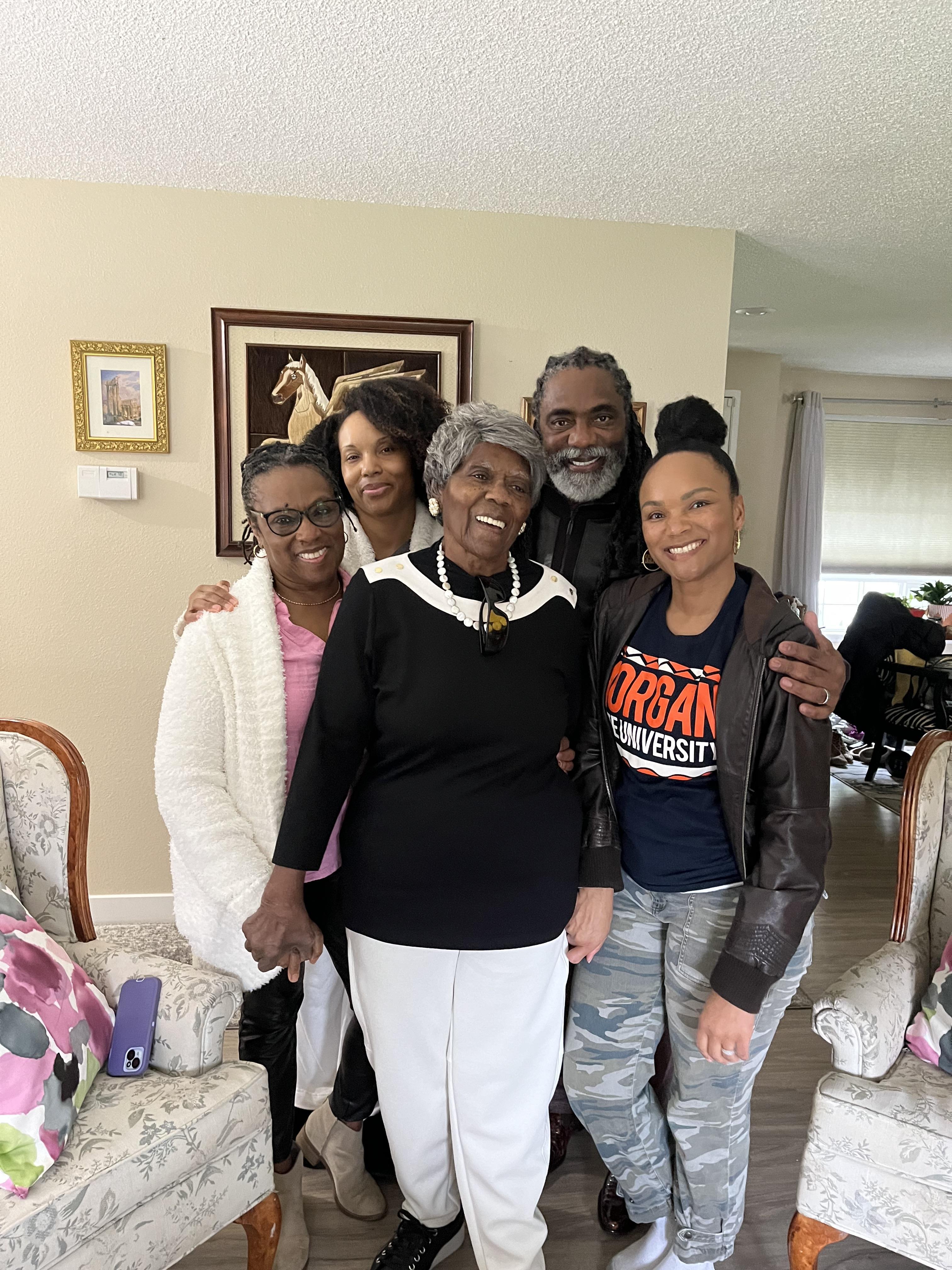 Five family members pose together, showing joy and connection during a gathering at home.