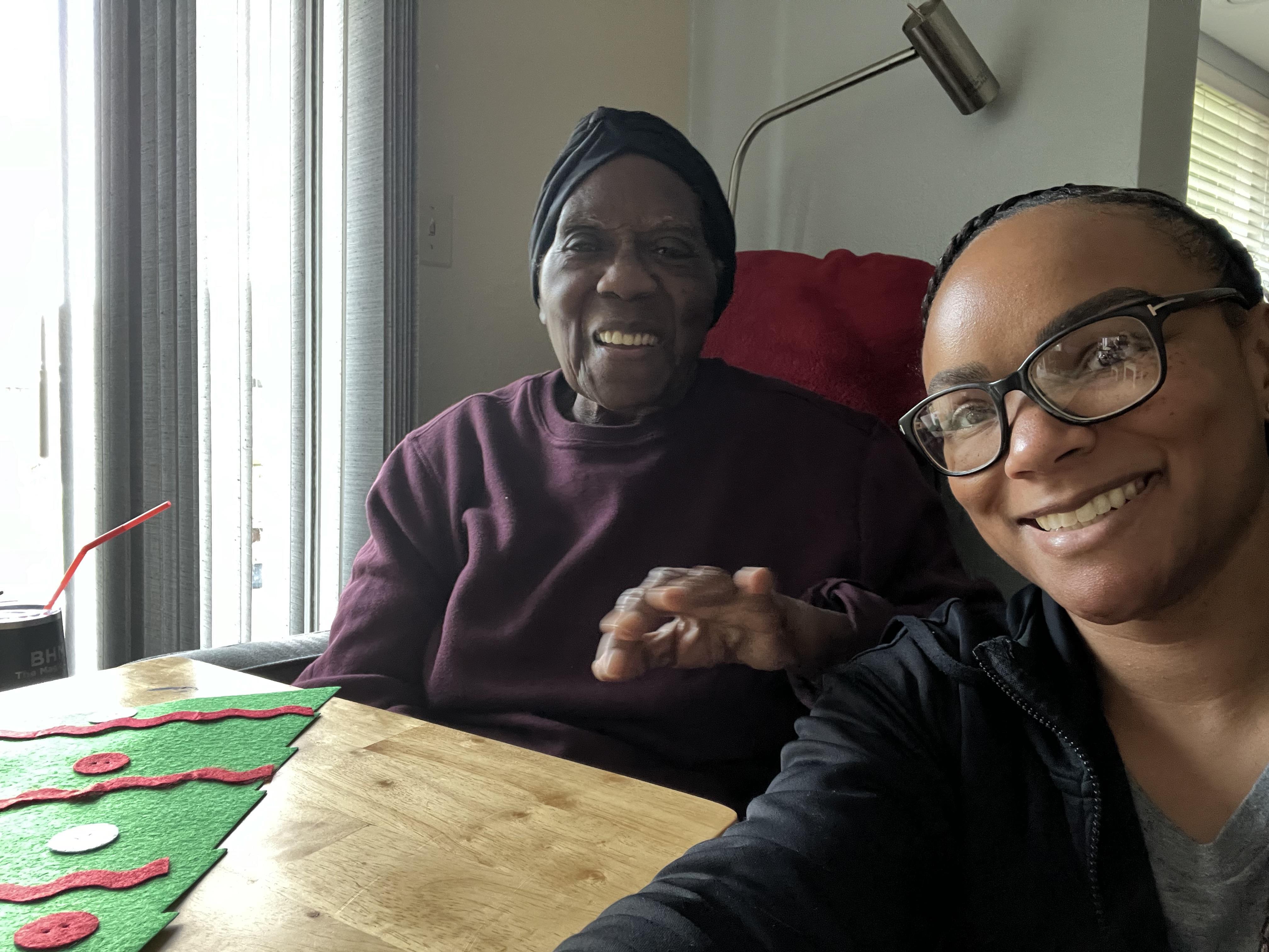 Two generations smile together at a wooden table, sharing a joyful moment in a bright room.