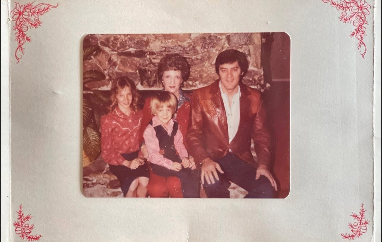 A family sits together in a cozy living room, dressed in vibrant 1970s fashion, smiling warmly.