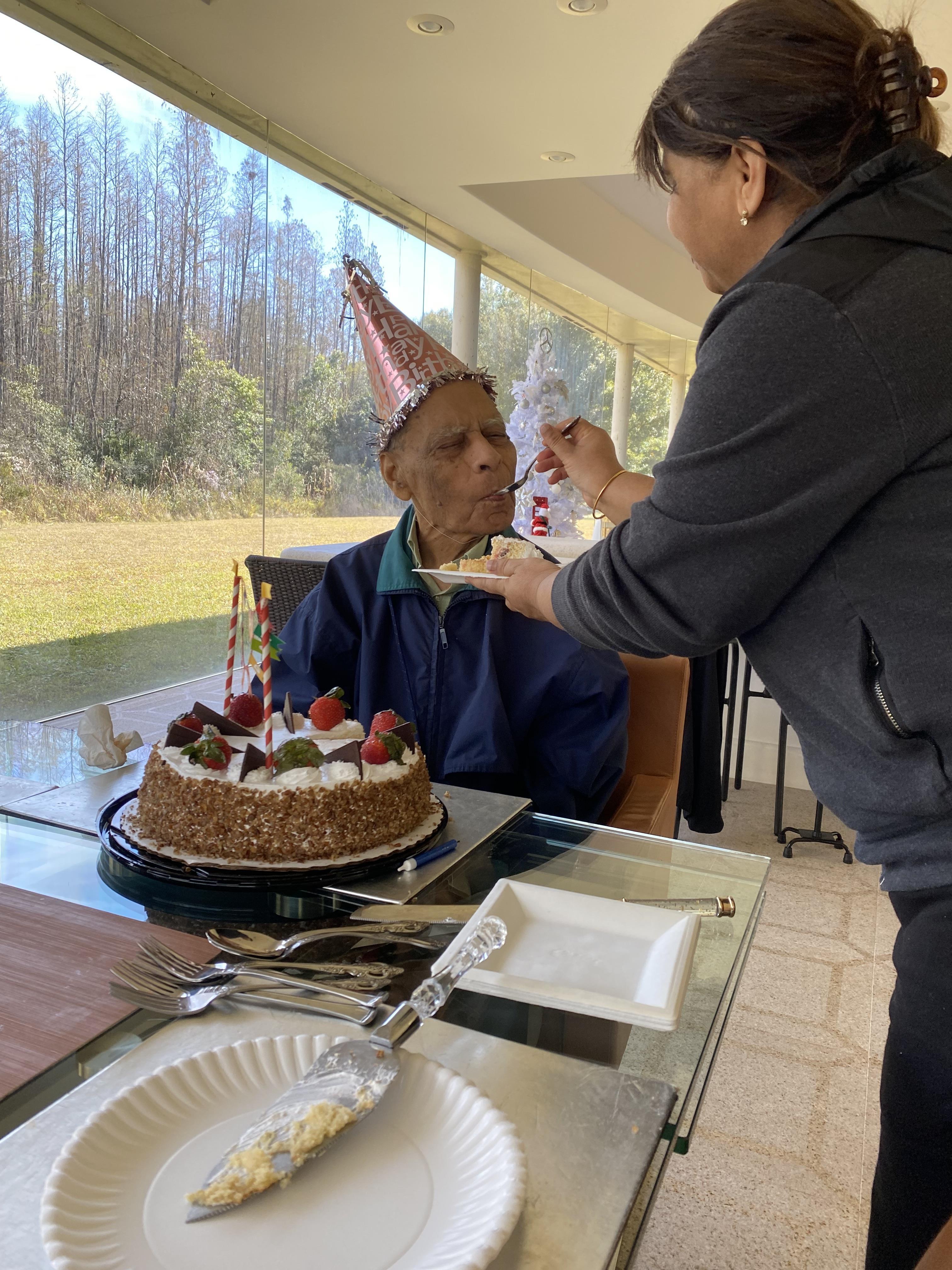 Family gathers to celebrate a birthday with cake and laughter in a serene outdoor environment.