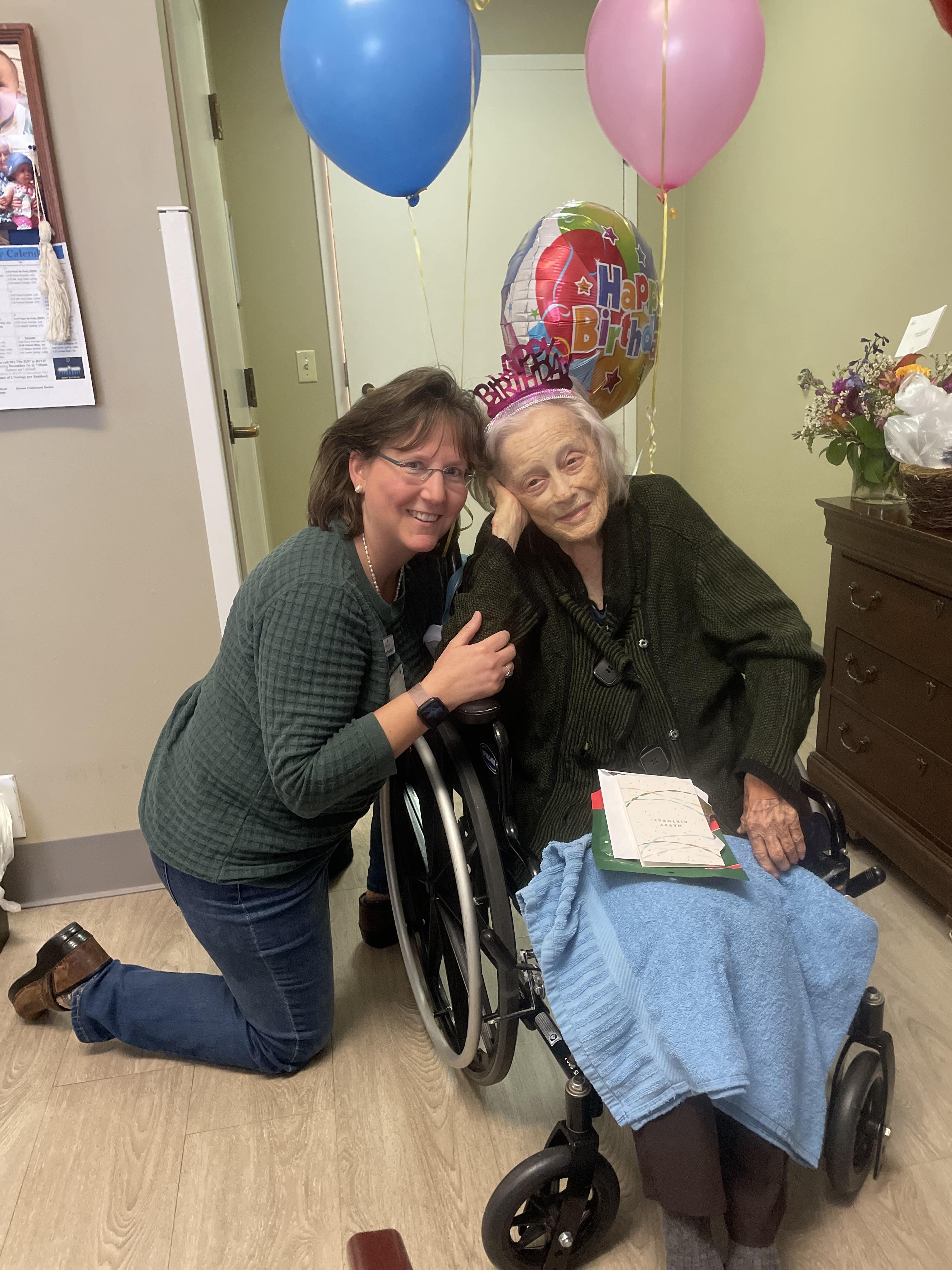Friends celebrate a joyful moment with an elderly woman in a wheelchair during a festive occasion.