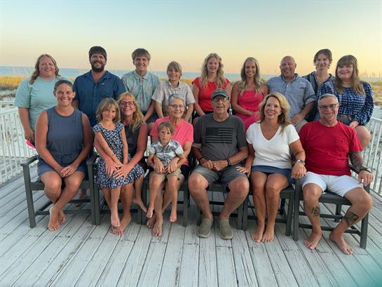 Group of friends and family gathered on a beach deck during a beautiful sunset, smiling happily.