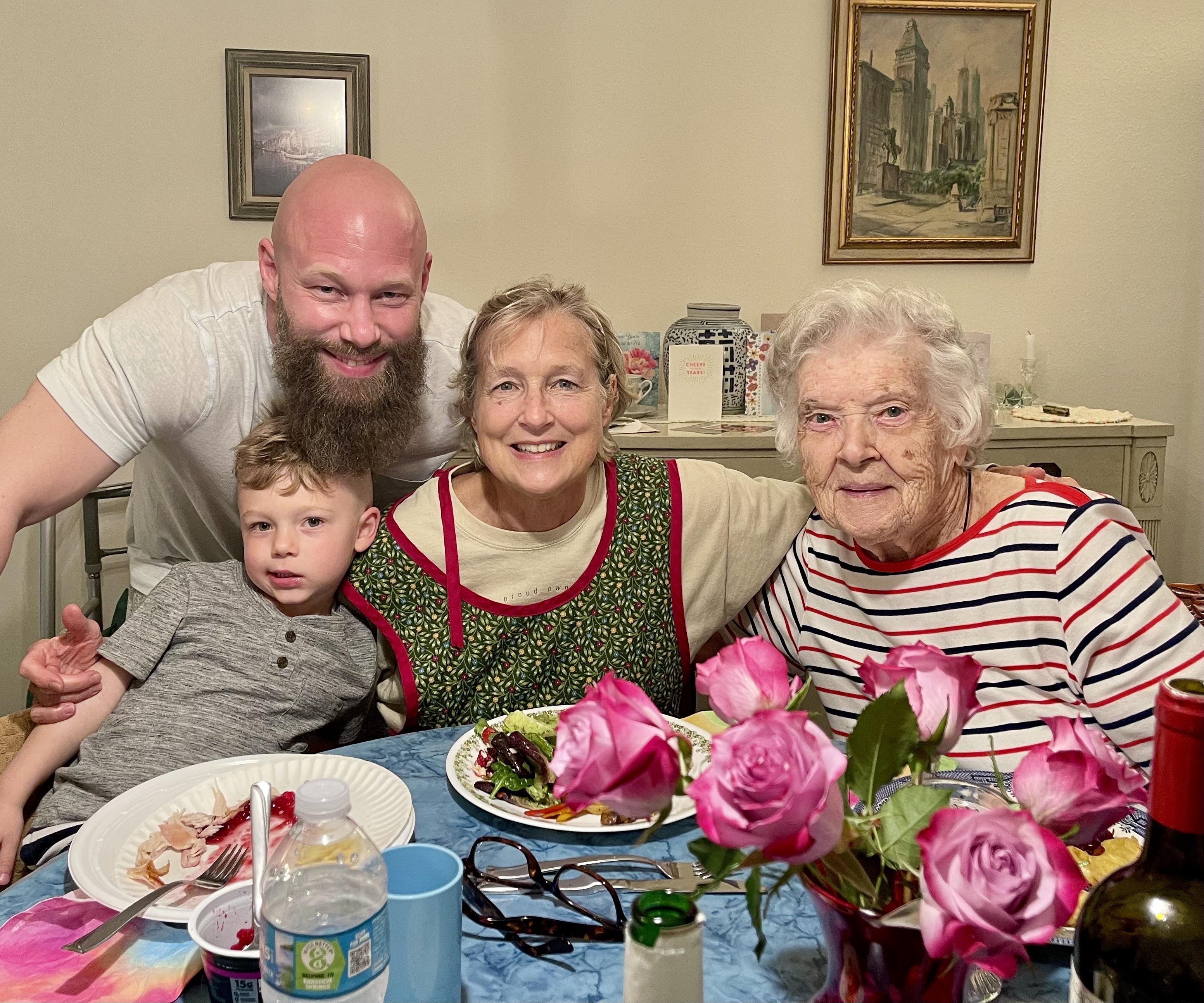 Four family members cherish a moment around a table filled with food and fresh roses.