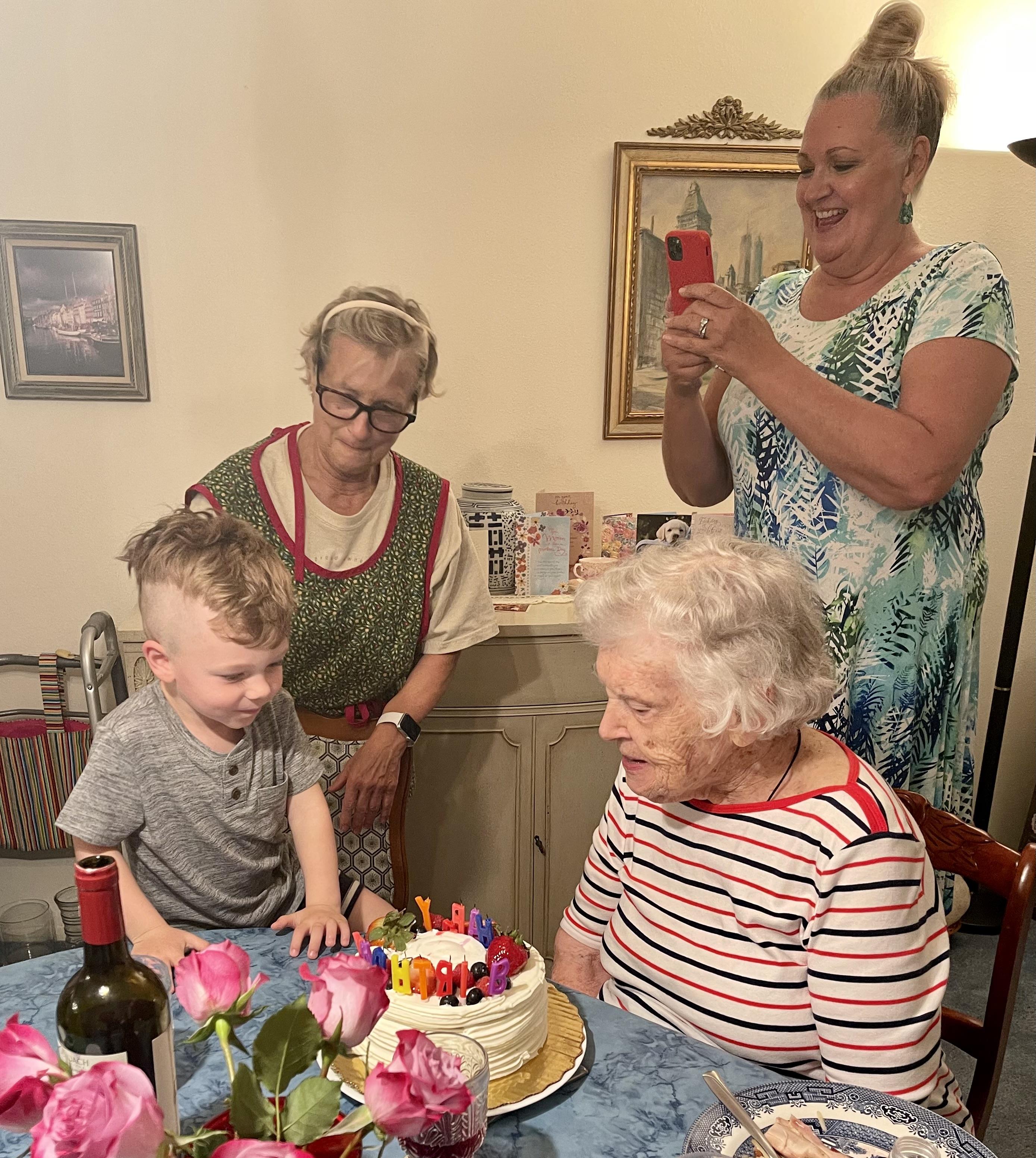Kids and adults enjoy a birthday with cake, flowers, and happy moments in a cozy room.