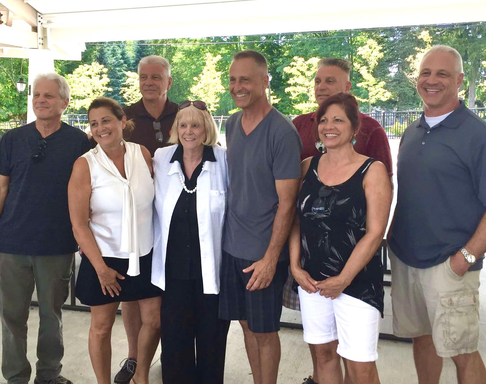 A group of joyful family members pose together under a tent during a sunny gathering in a park.