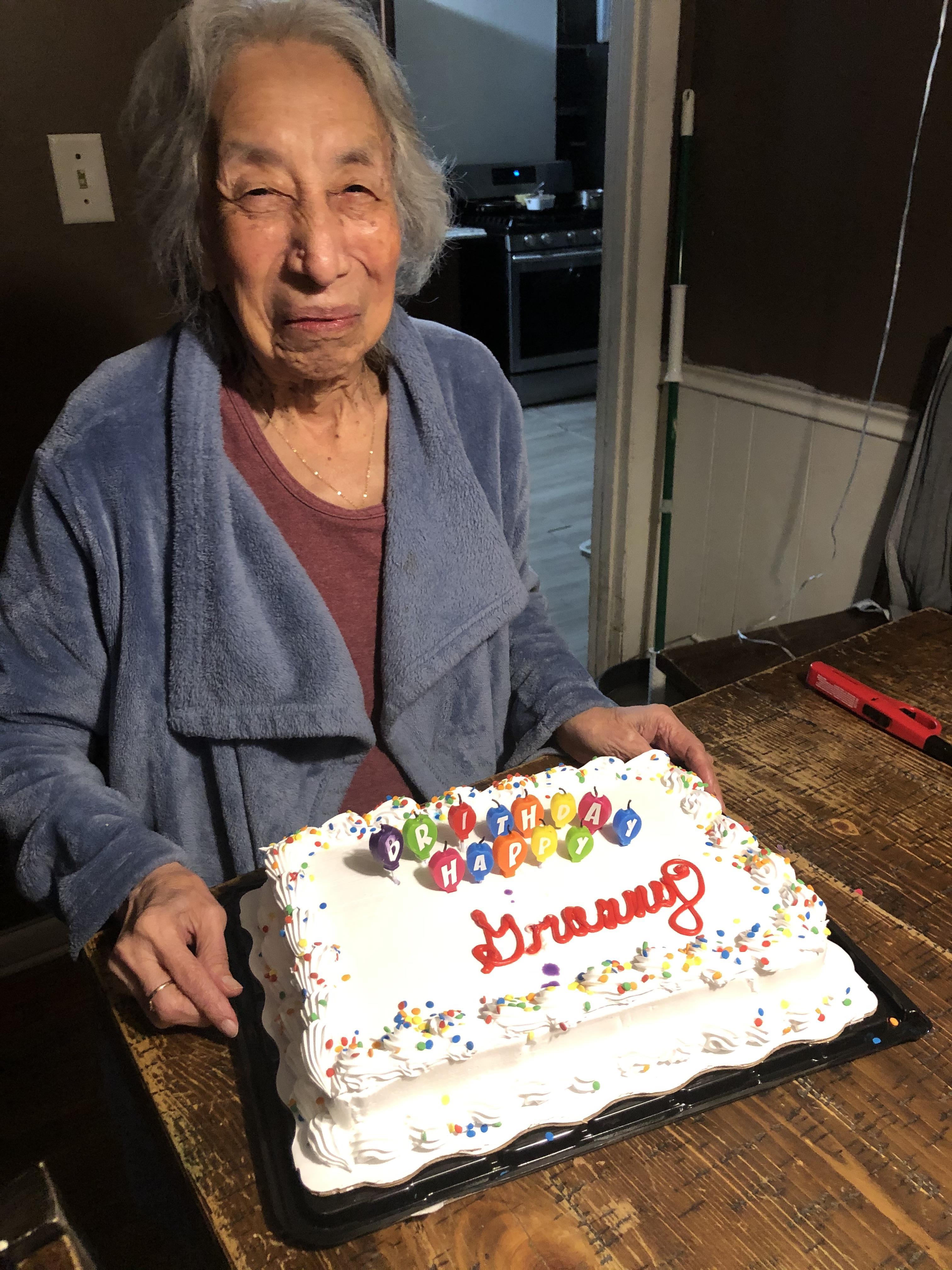 A woman joyfully poses with a birthday cake, celebrating her special day at home with family.
