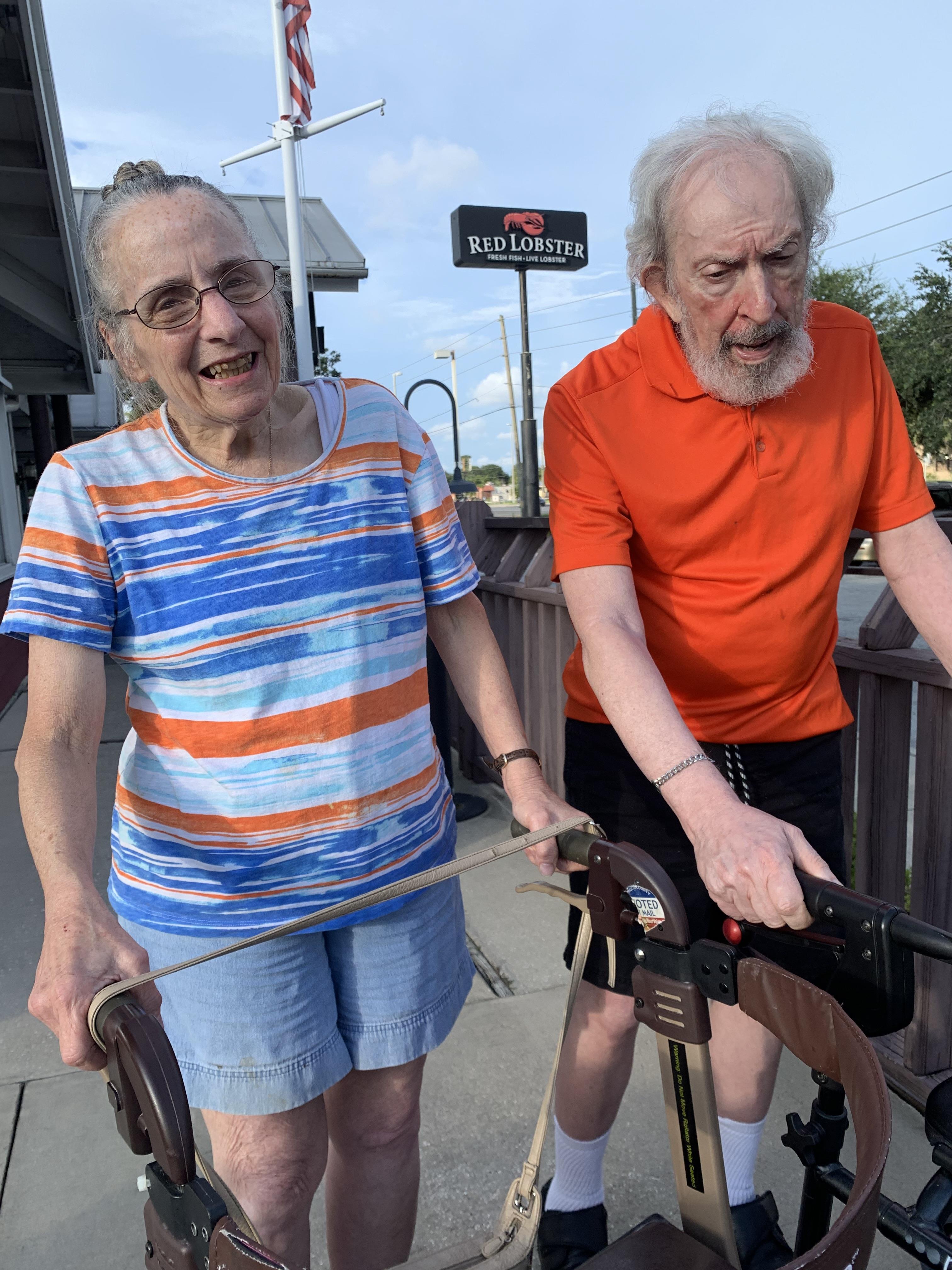 Two seniors stroll happily along the sidewalk, enjoying comfortable weather and companionship.