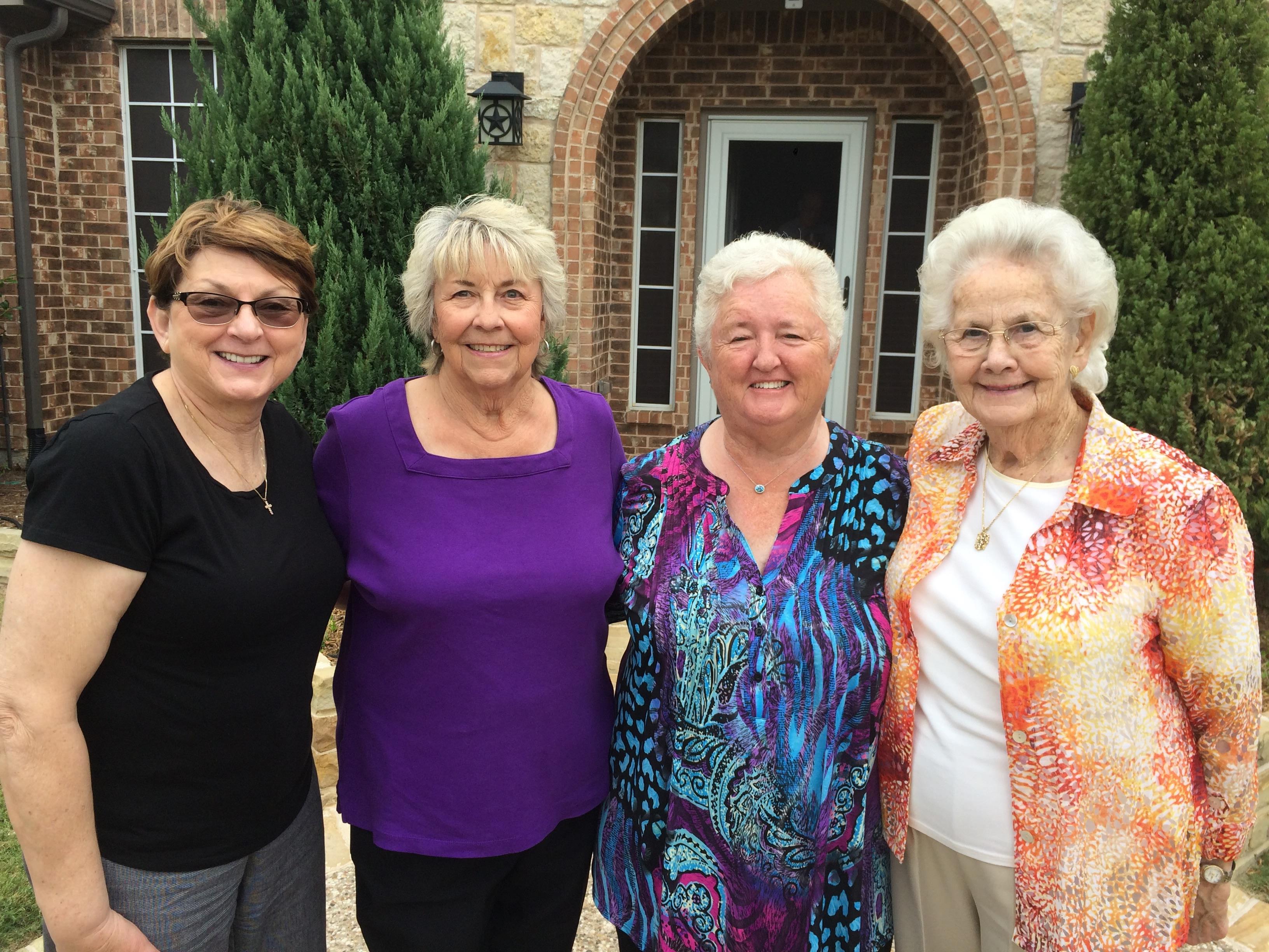 Four friends smile together at a gathering outside a lovely home, enjoying their time.