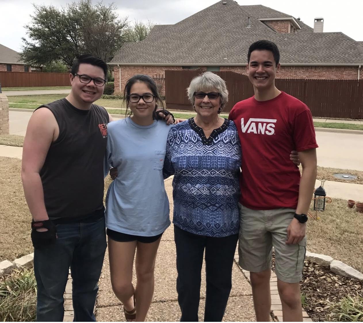 Four people stand together outside a house on a cloudy day, enjoying a family moment.