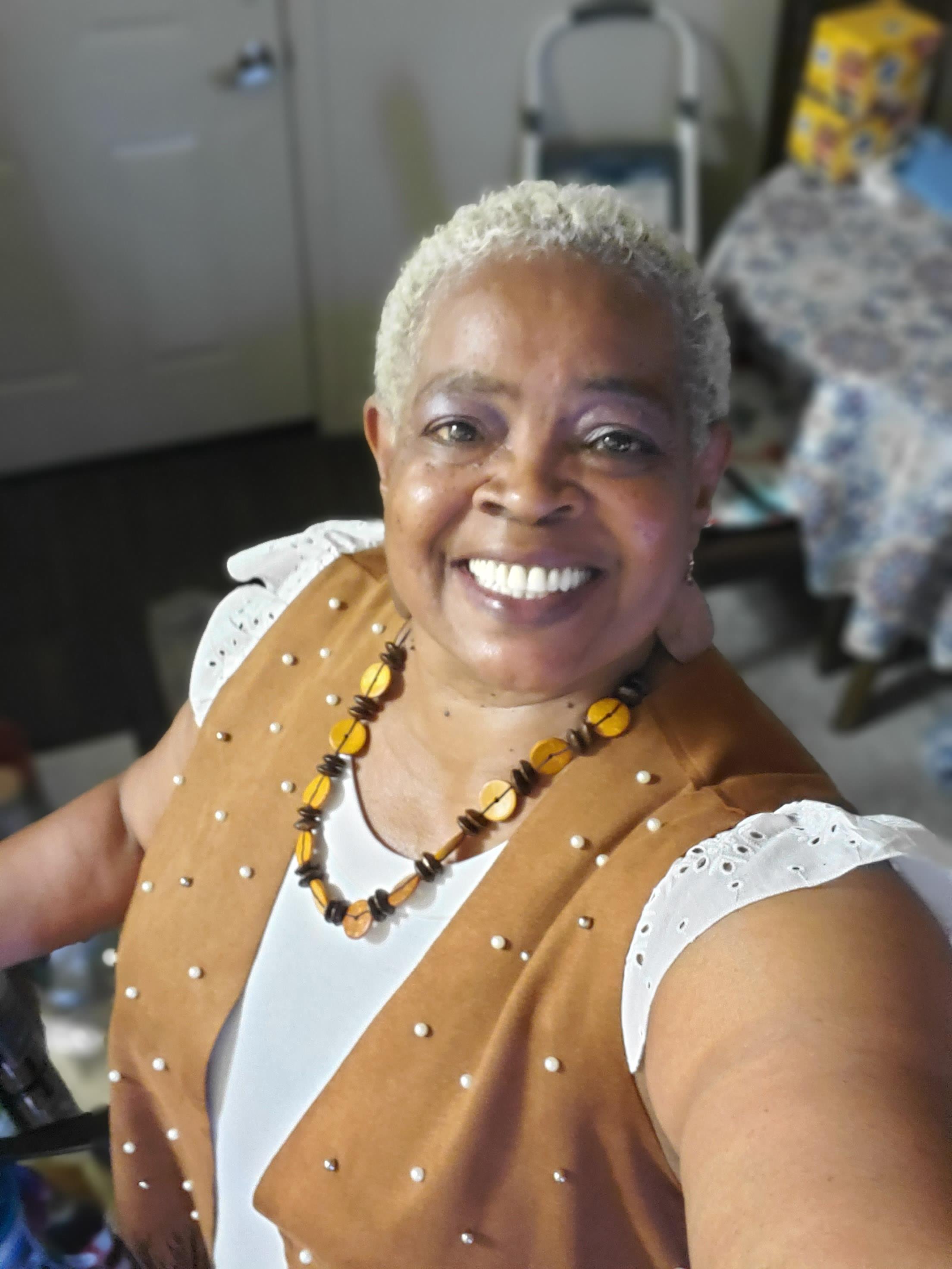 Older woman with short gray hair smiles warmly while showcasing her unique jewelry collection.