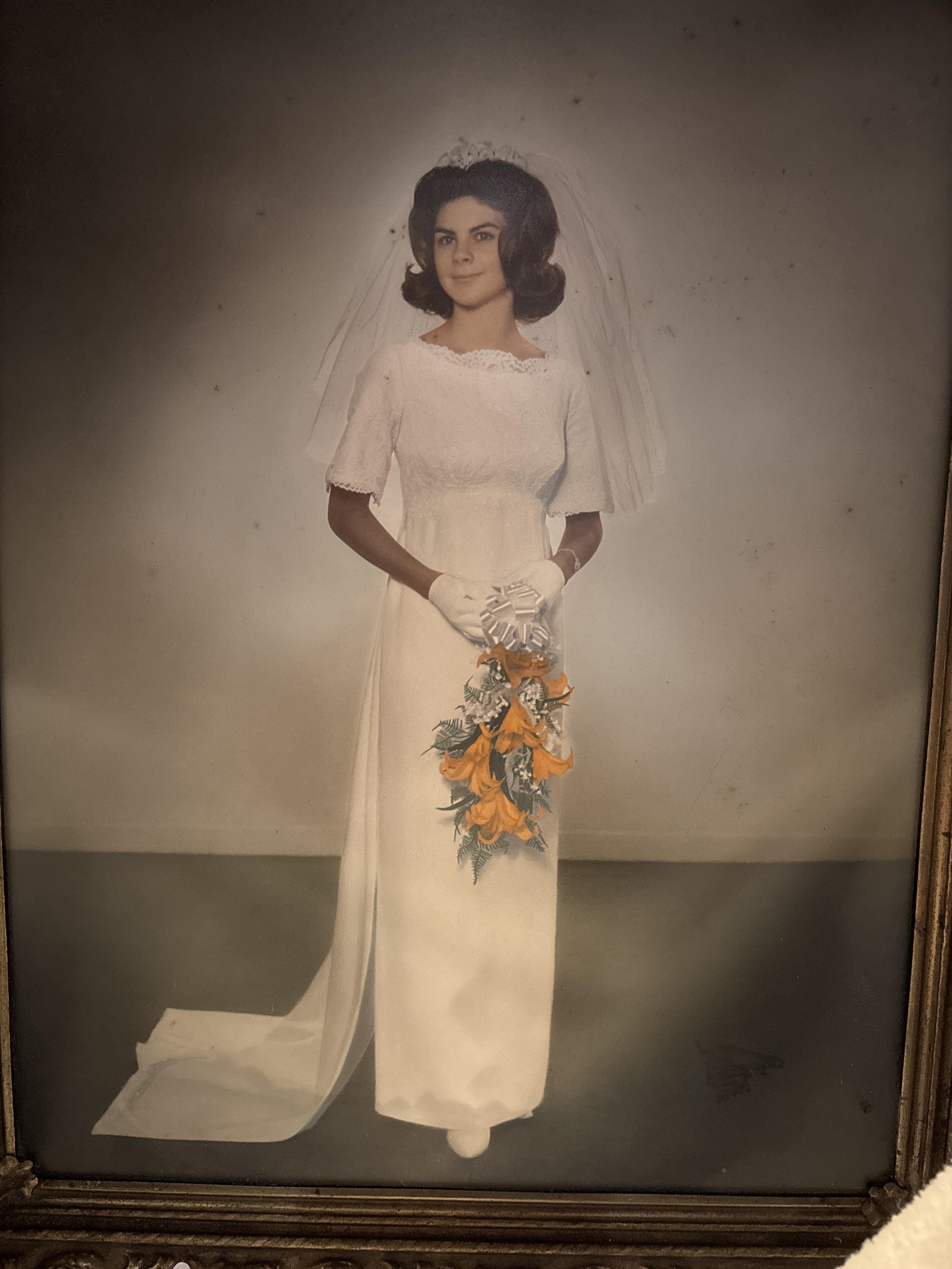 A woman stands elegantly in a beautiful wedding dress adorned with flowers, holding a bouquet.
