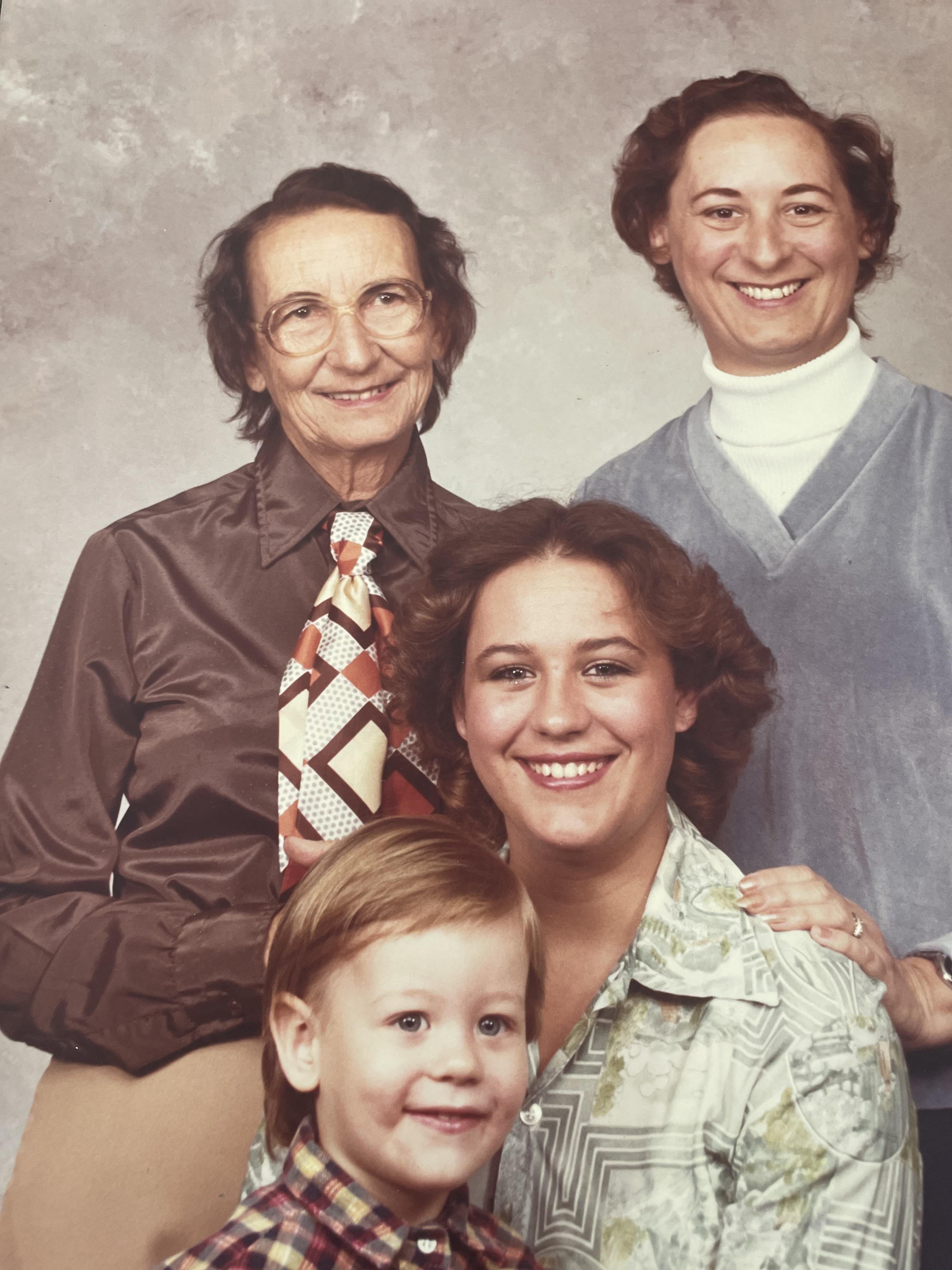 A joyous family portrait captures four generations smiling together in a studio.