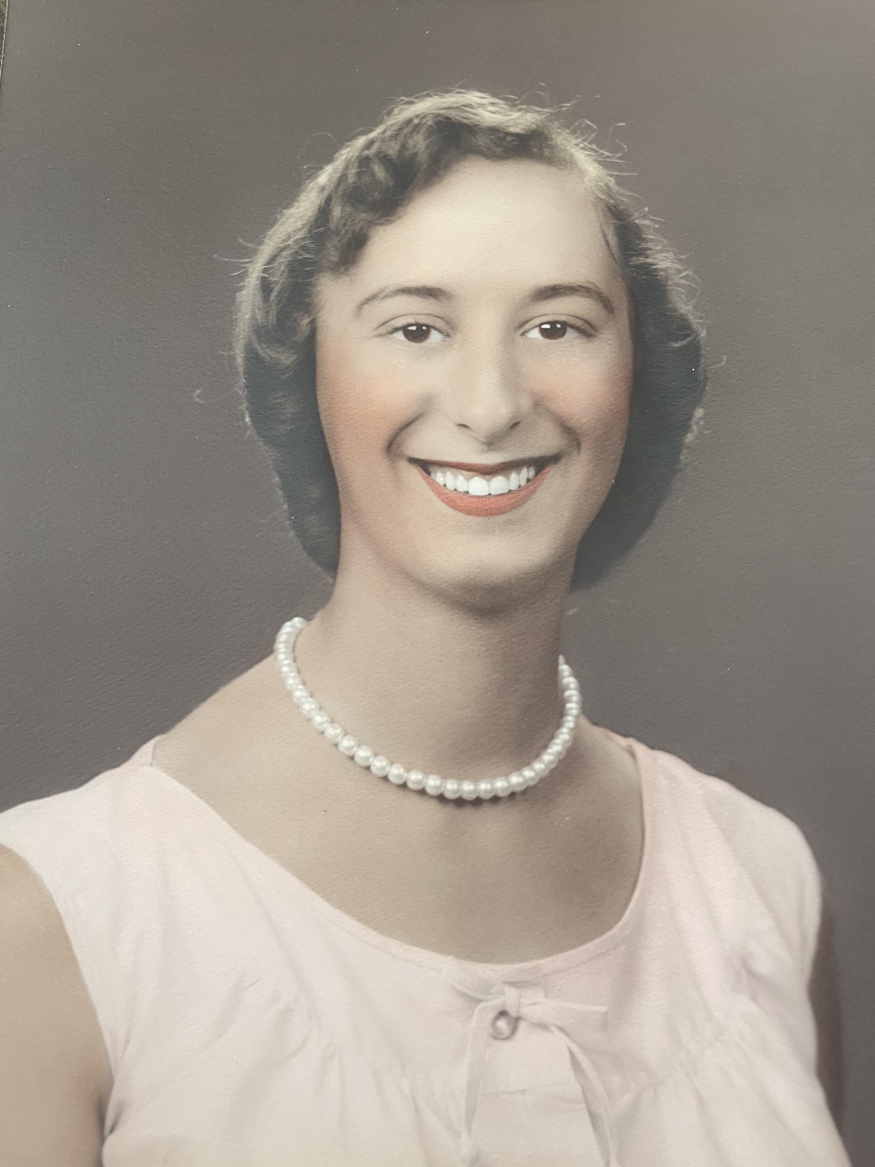 A woman with a joyful expression is adorned with a pearl necklace in this vintage portrait.